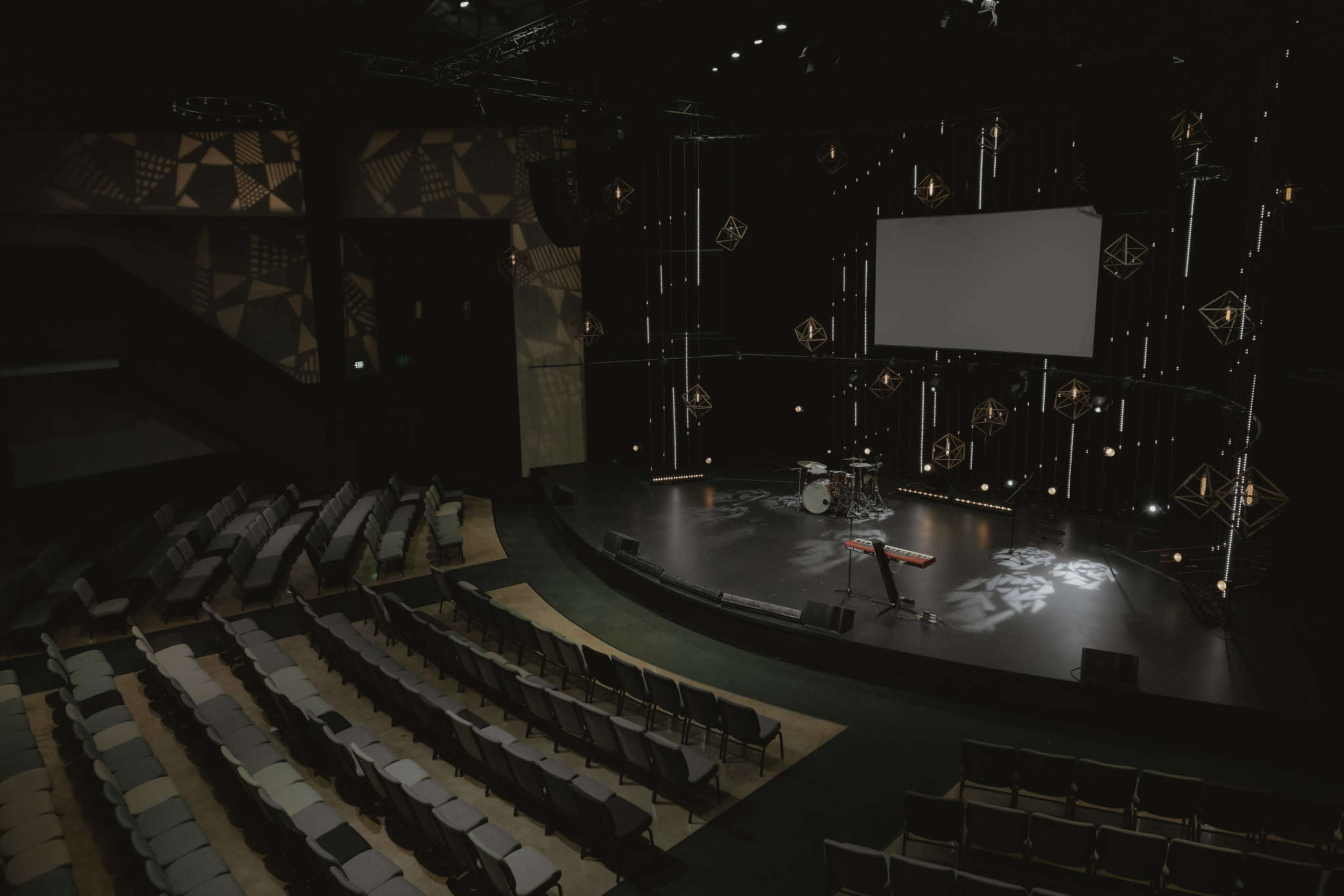 An empty auditorium stage with a drum set and keyboard, surrounded by rows of seats.