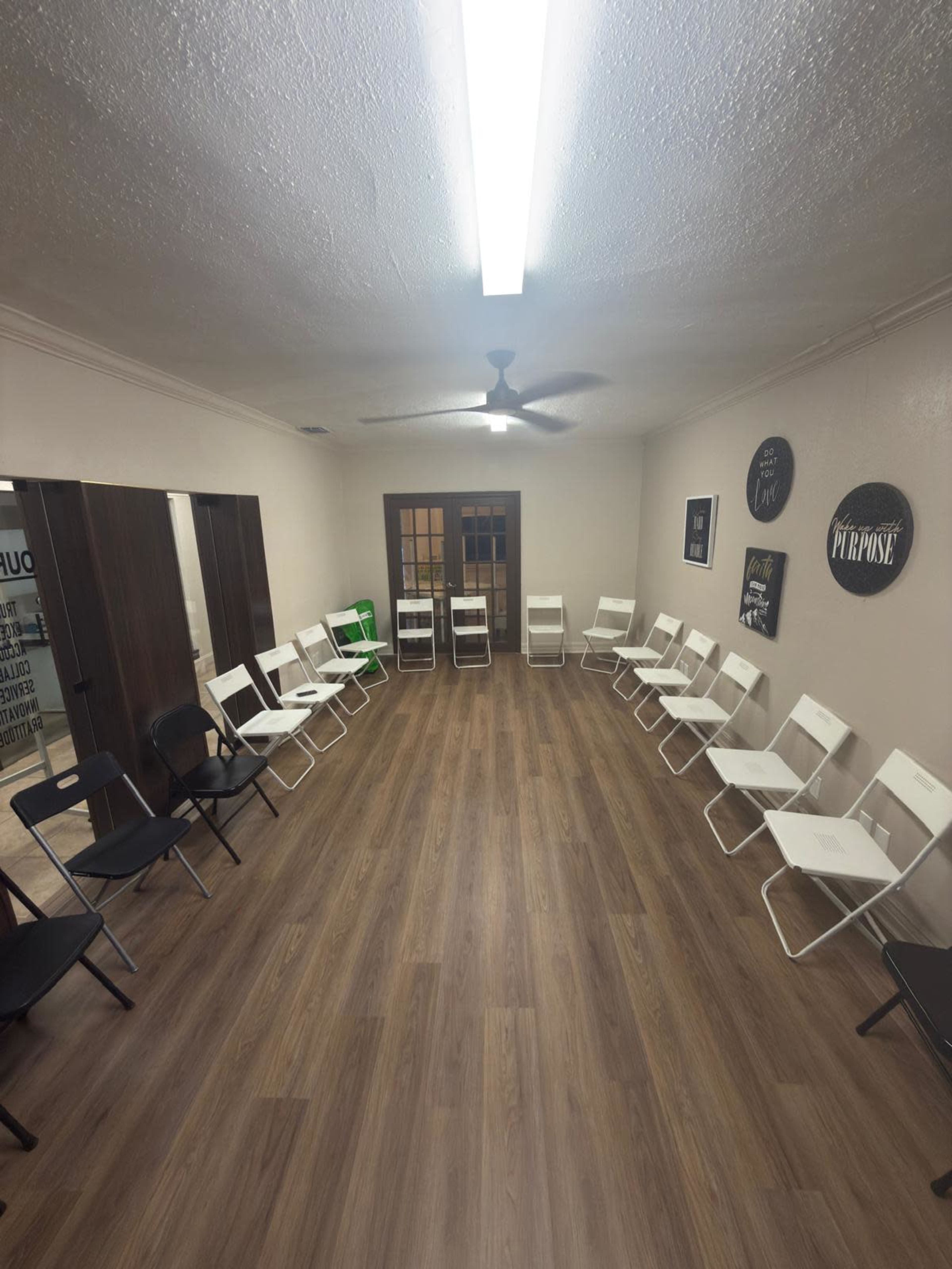 The image shows a room with wooden flooring arranged in a circular layout with white and black folding chairs.