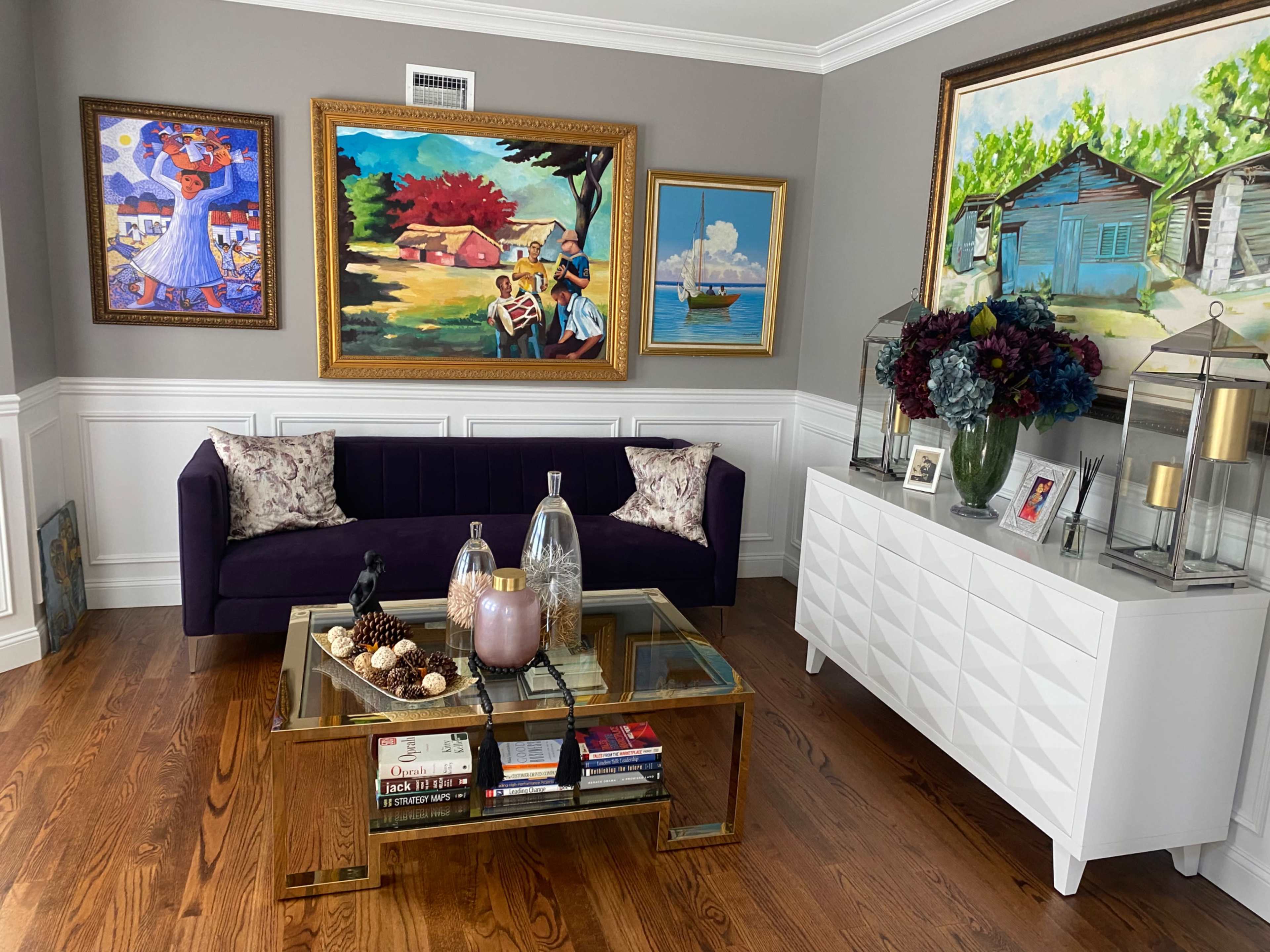 A living room featuring a dark purple sofa, a glass coffee table with decorative items, and several framed artworks on the walls.