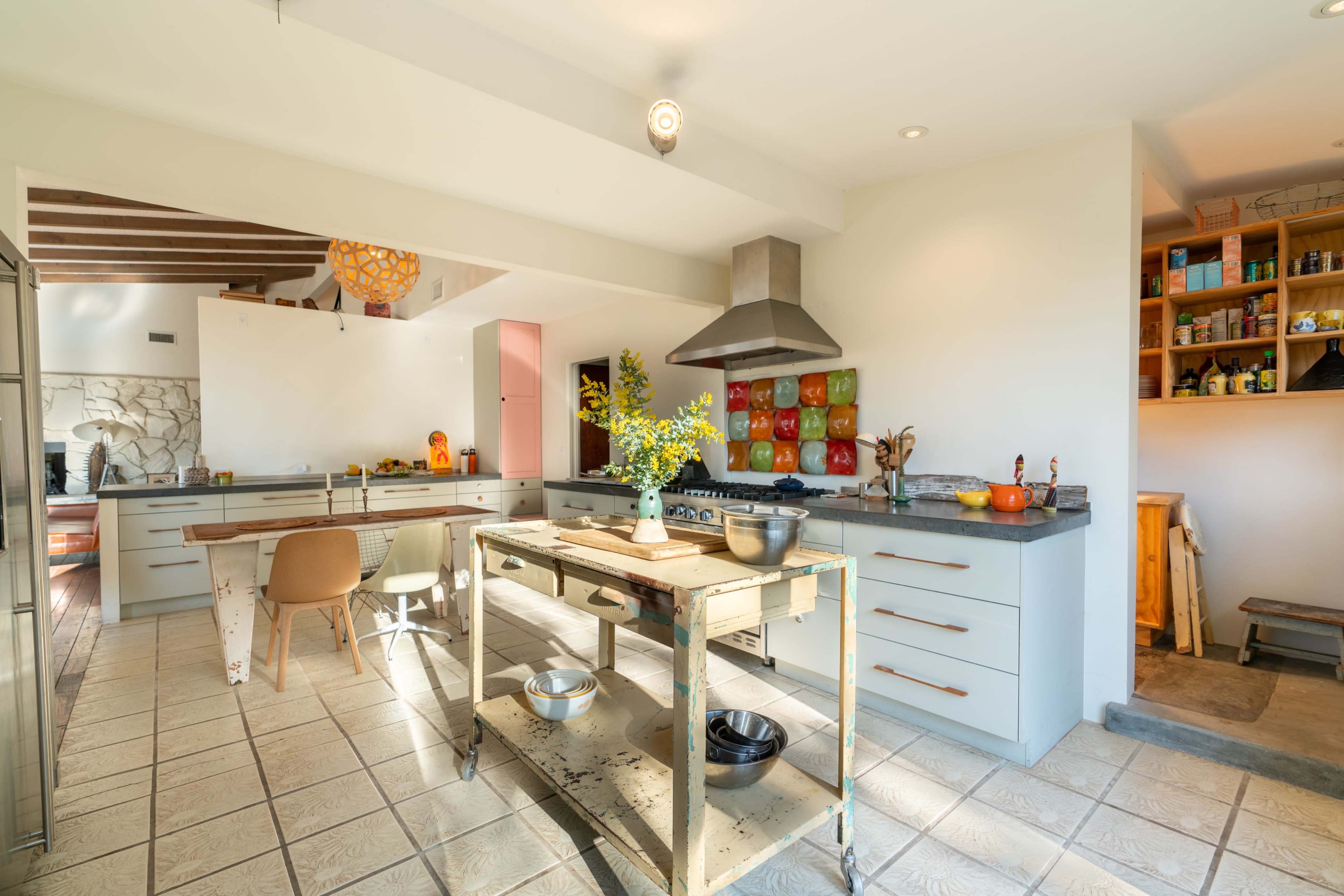 A spacious kitchen features a central table, modern appliances, and colorful wall art, with natural light illuminating the space.