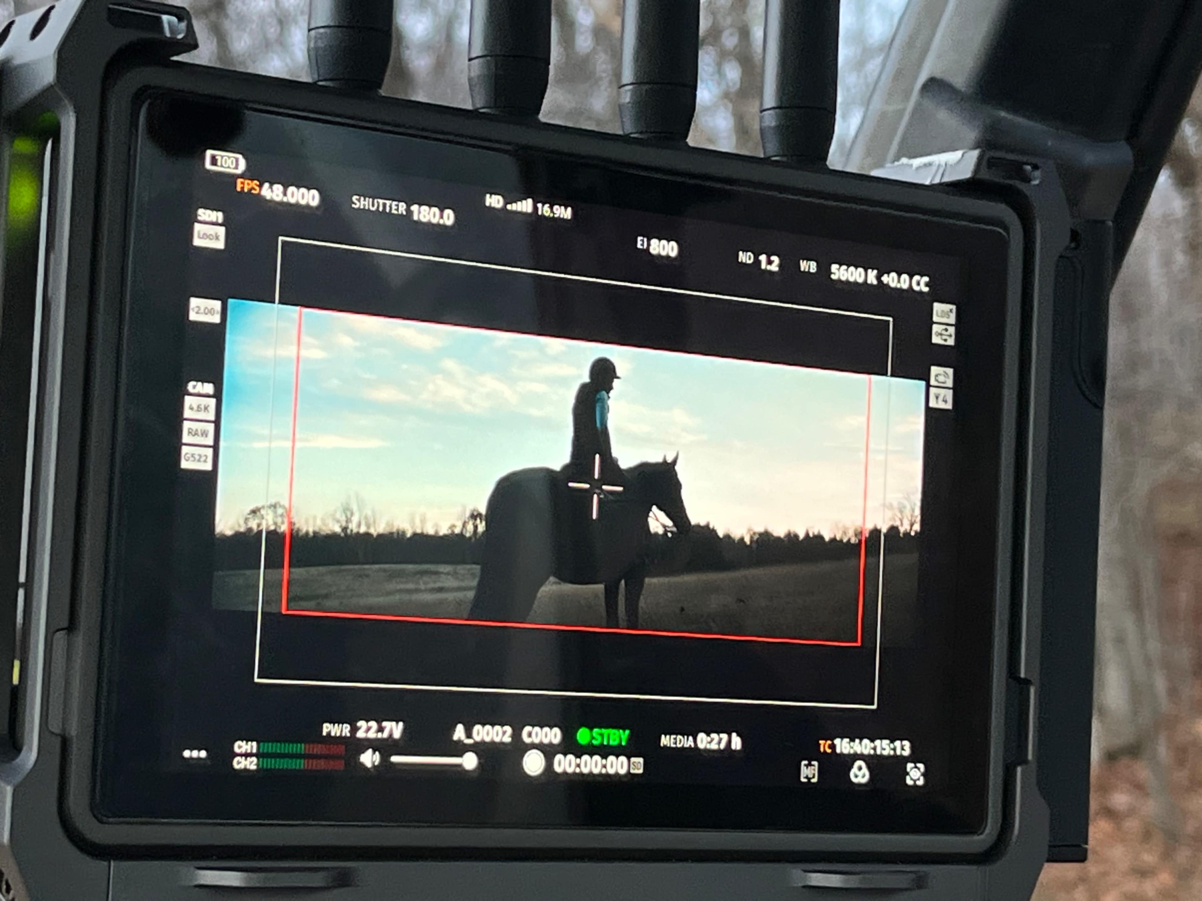 A camera monitor displaying a silhouette of a person on a horse against a sunset background.