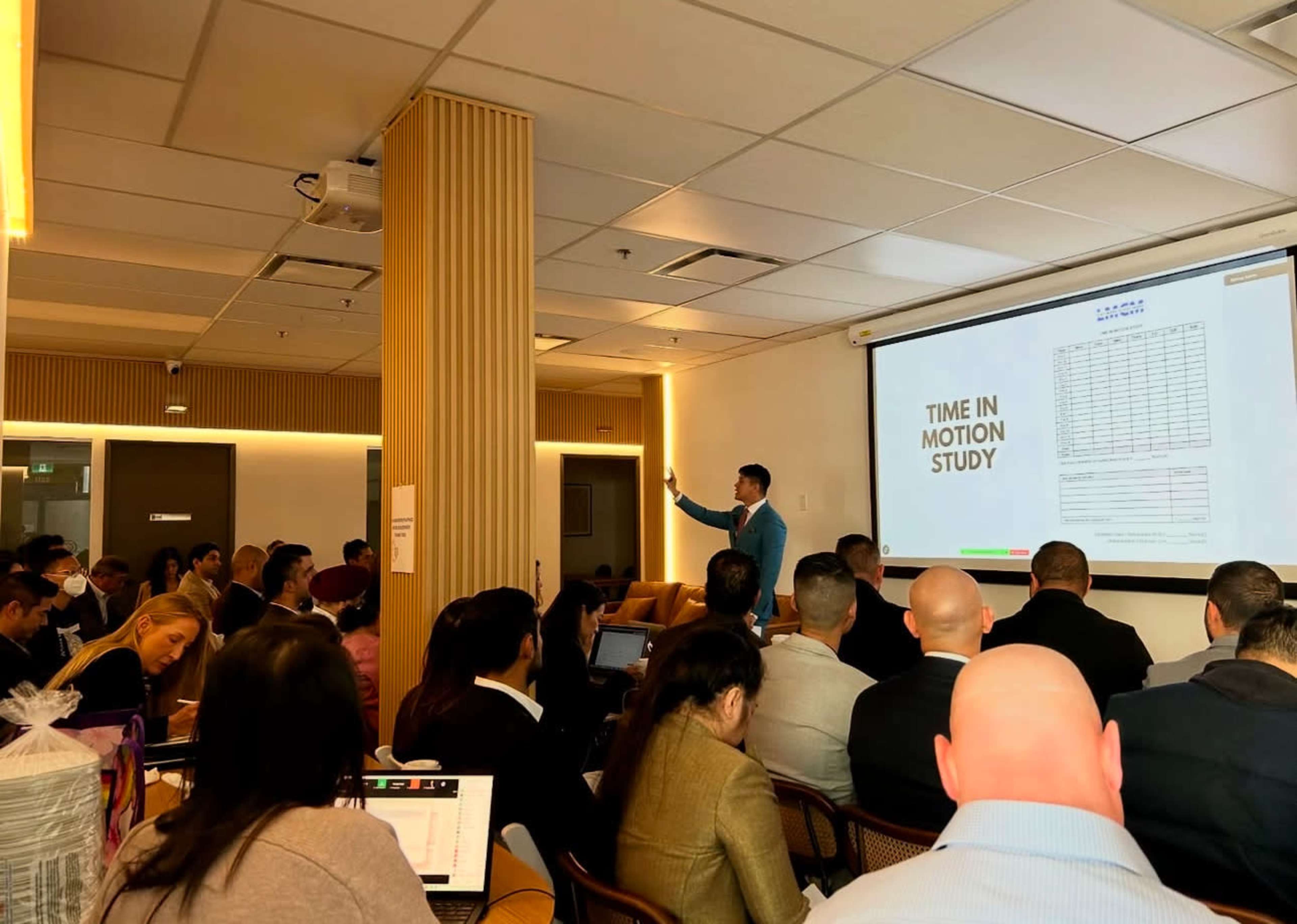 A speaker presents a "Time in Motion Study" to an audience seated in a conference room.