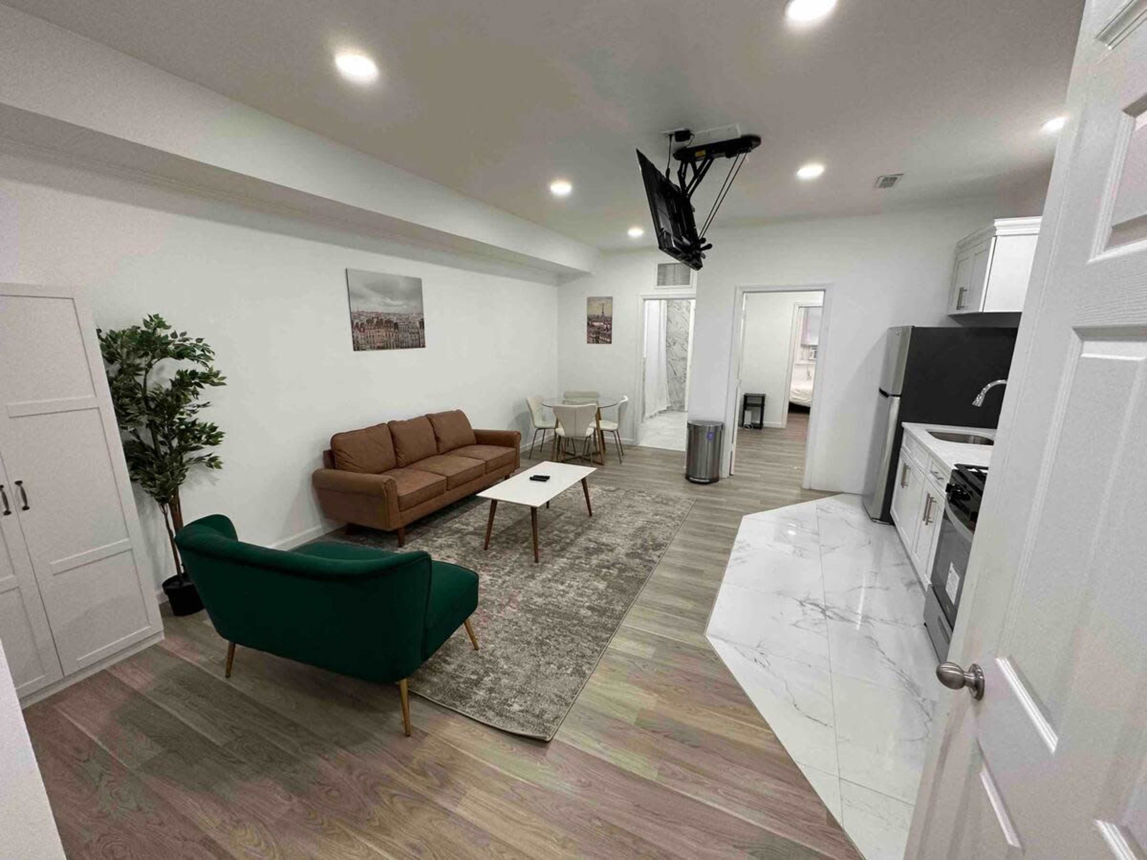 A modern living space features a green sofa, a brown couch, a coffee table, and a kitchenette area with marble flooring.