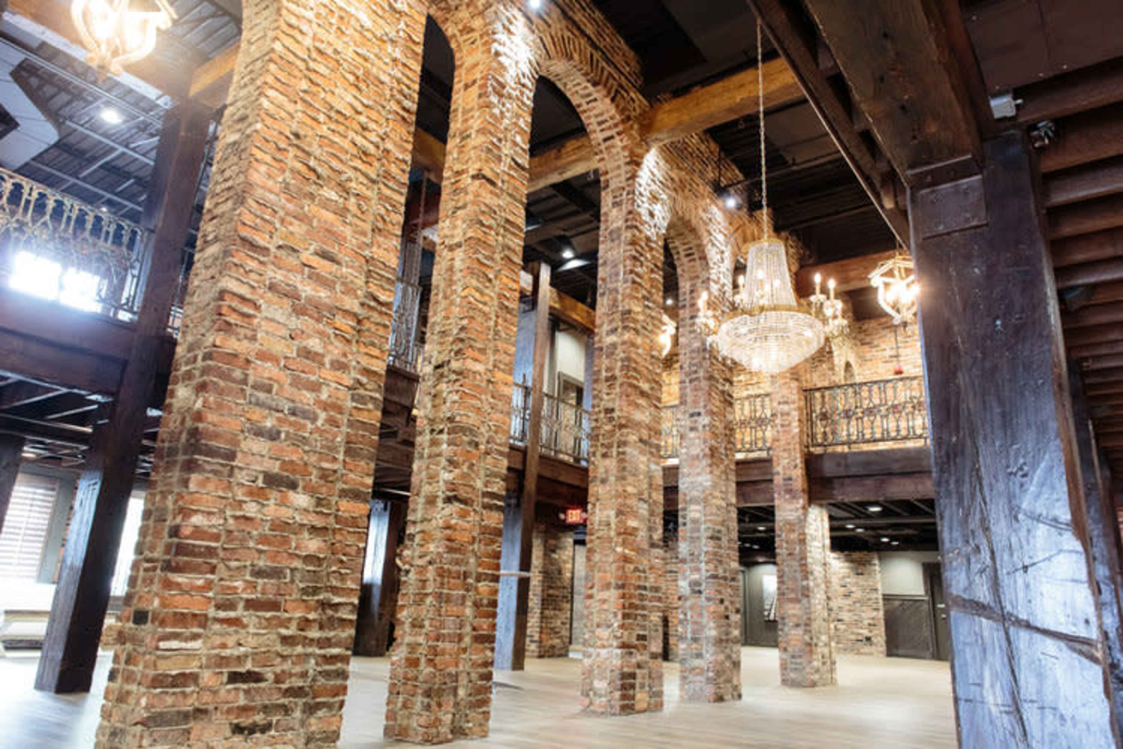 A spacious interior with tall brick pillars, wooden beams, and chandeliers illuminating the area.