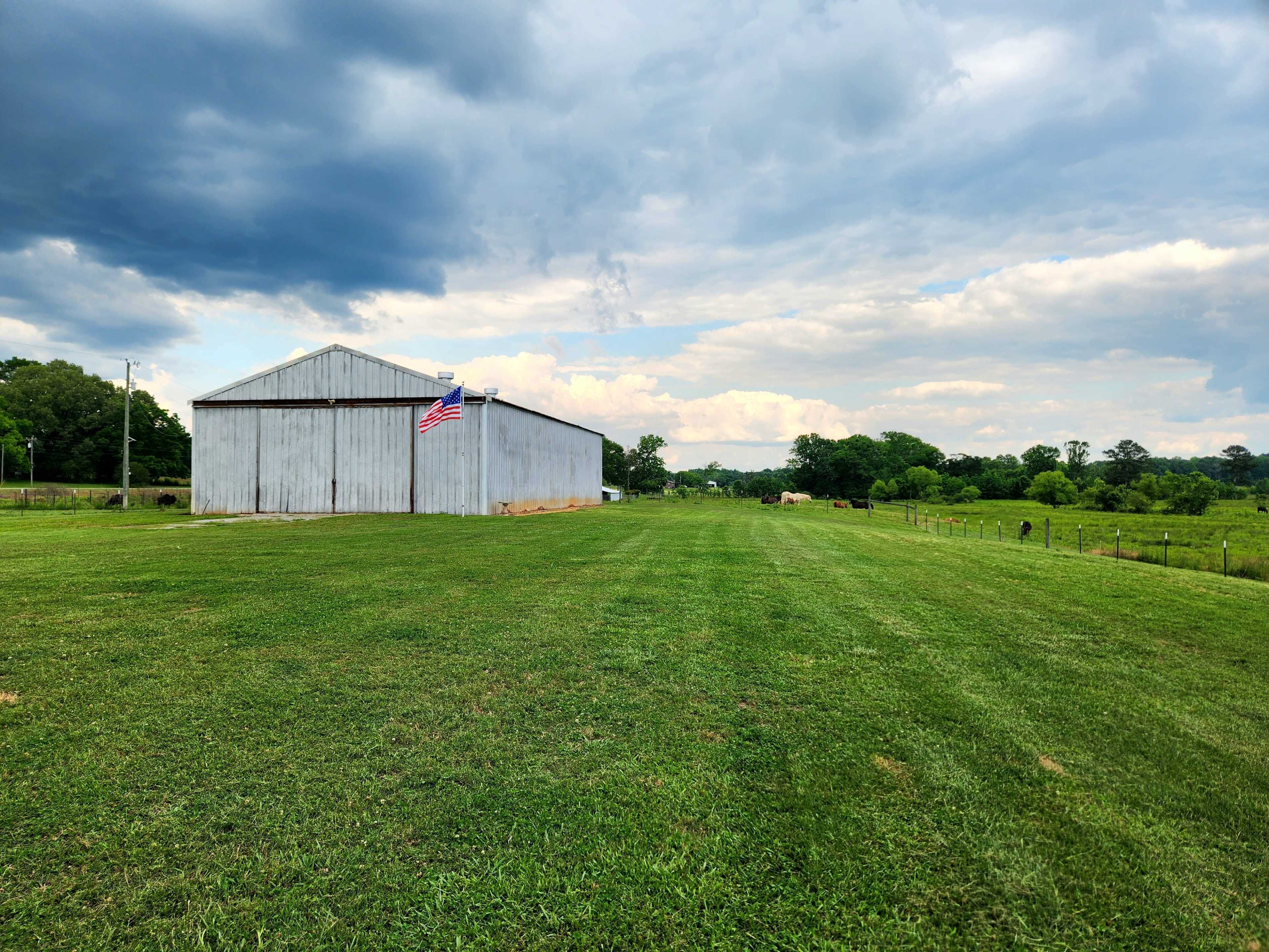 A metal barn with an American flag is set against a green field under a cloudy sky.