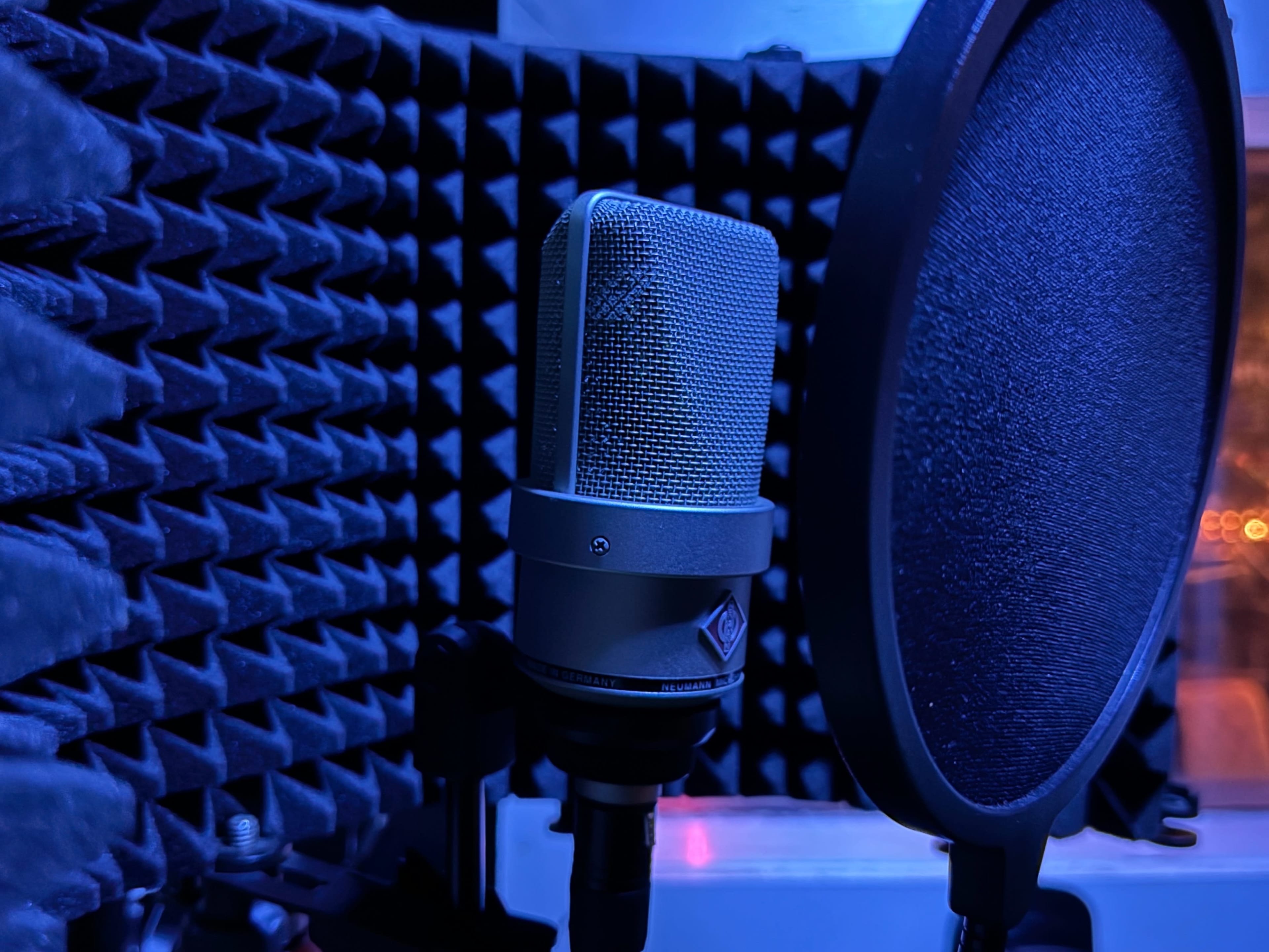 A microphone stands in front of a pop filter inside a soundproof recording booth.