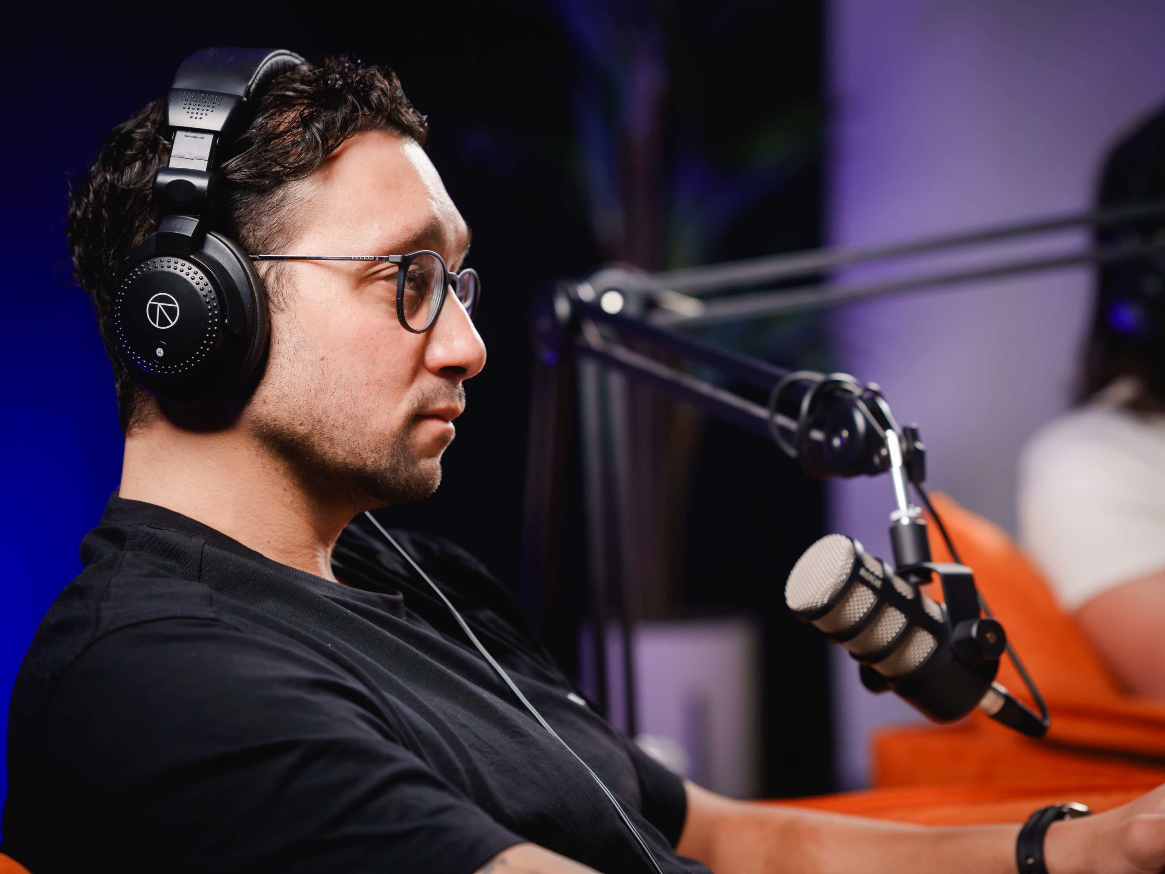 A man wearing headphones sits in profile next to a microphone in a studio setting.