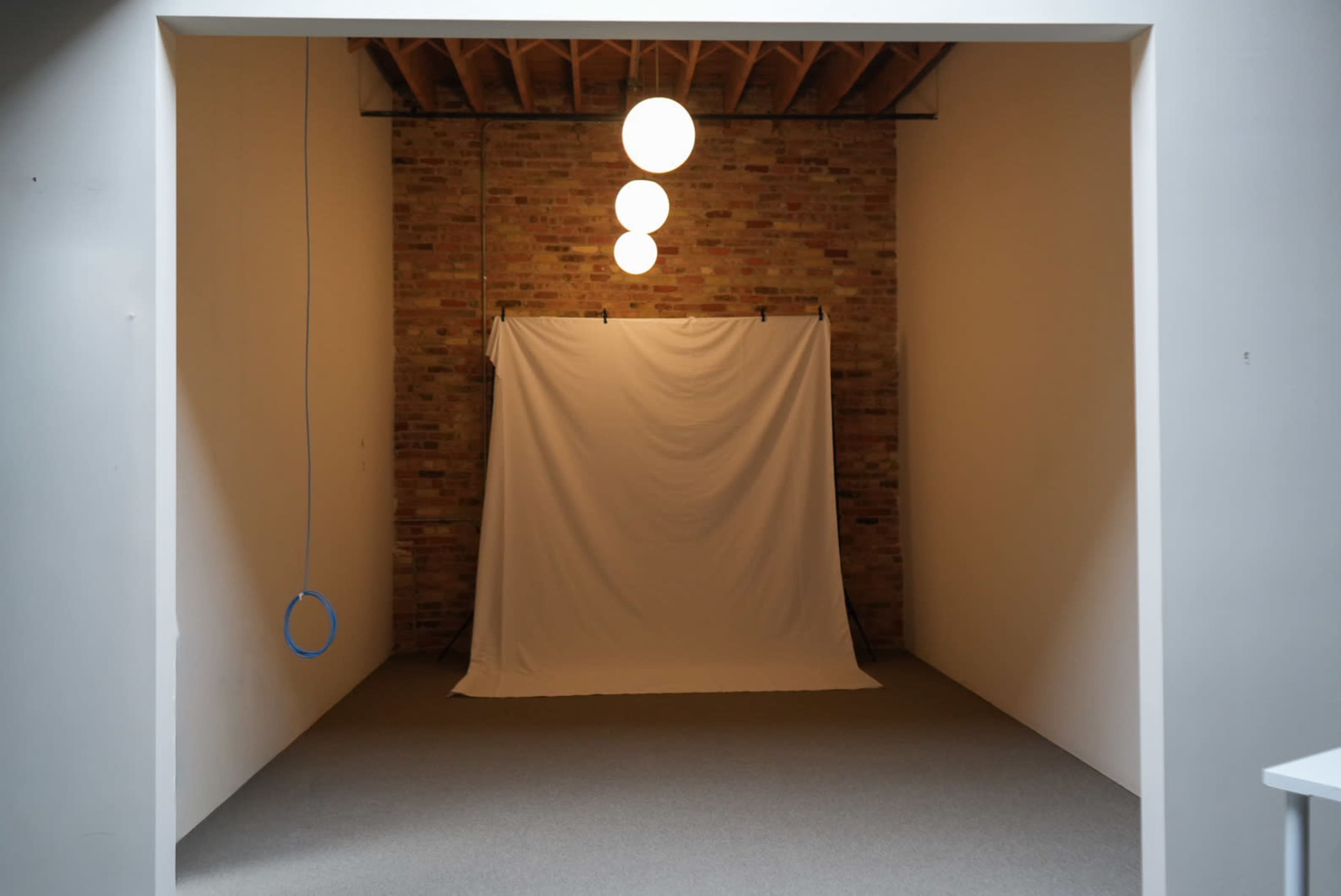 A plain studio space features a white backdrop against a brick wall, illuminated by three pendant lights.