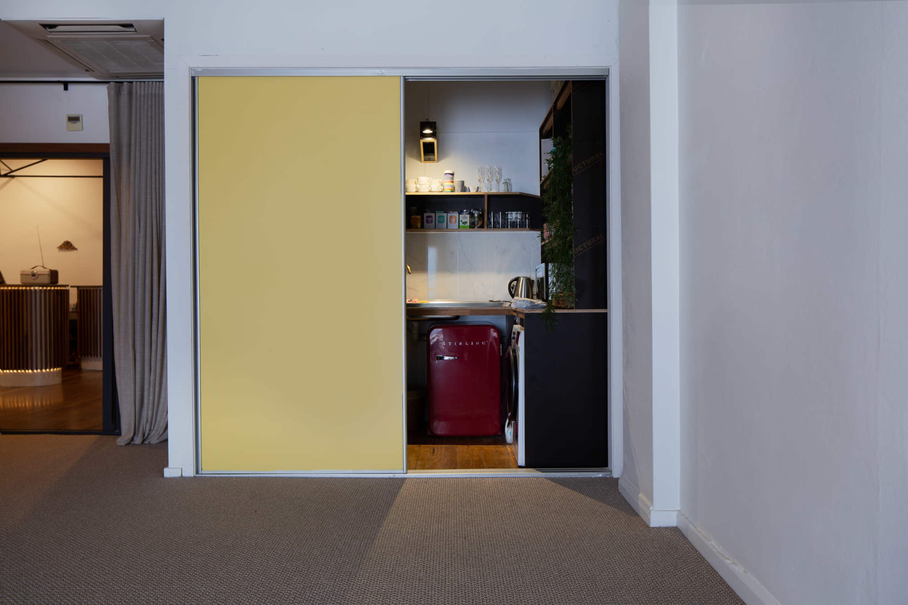 A partially open sliding door reveals a small kitchen area with a red refrigerator and various kitchen items visible on the shelves.