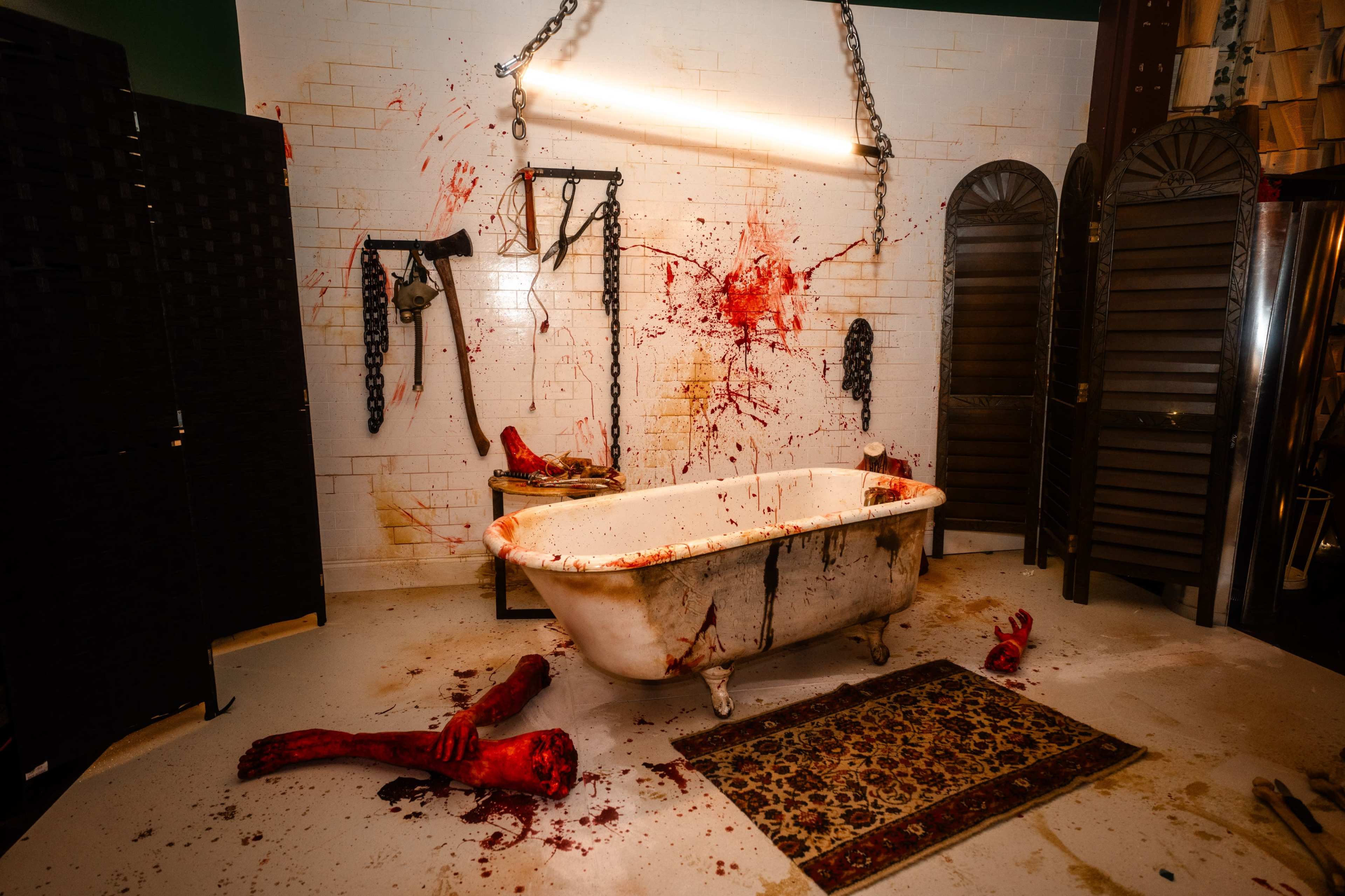 The scene depicts a grim, blood-splattered bathroom with a bathtub surrounded by gruesome props and chains.