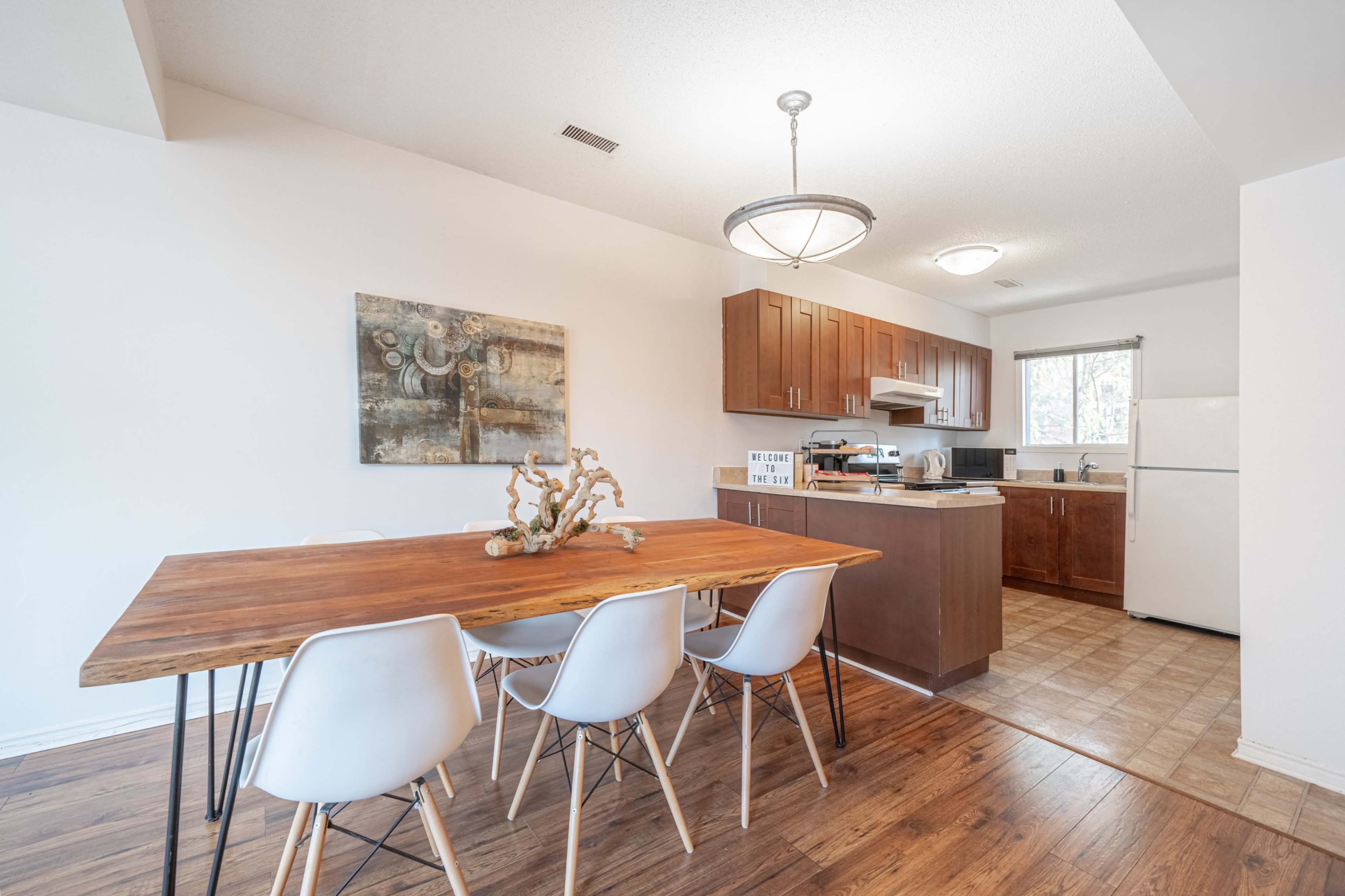 A dining area with a wooden table and chairs adjacent to a kitchen with brown cabinets and a white refrigerator.