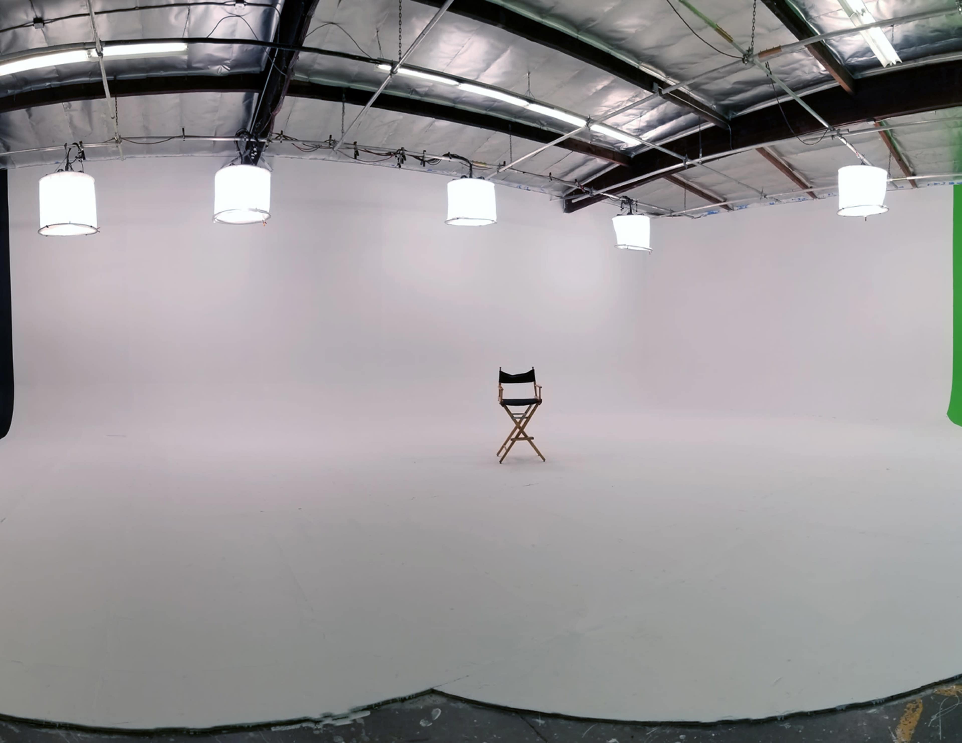 A spacious, empty studio featuring a single wooden director's chair under overhead lights, with white walls and a smooth floor.