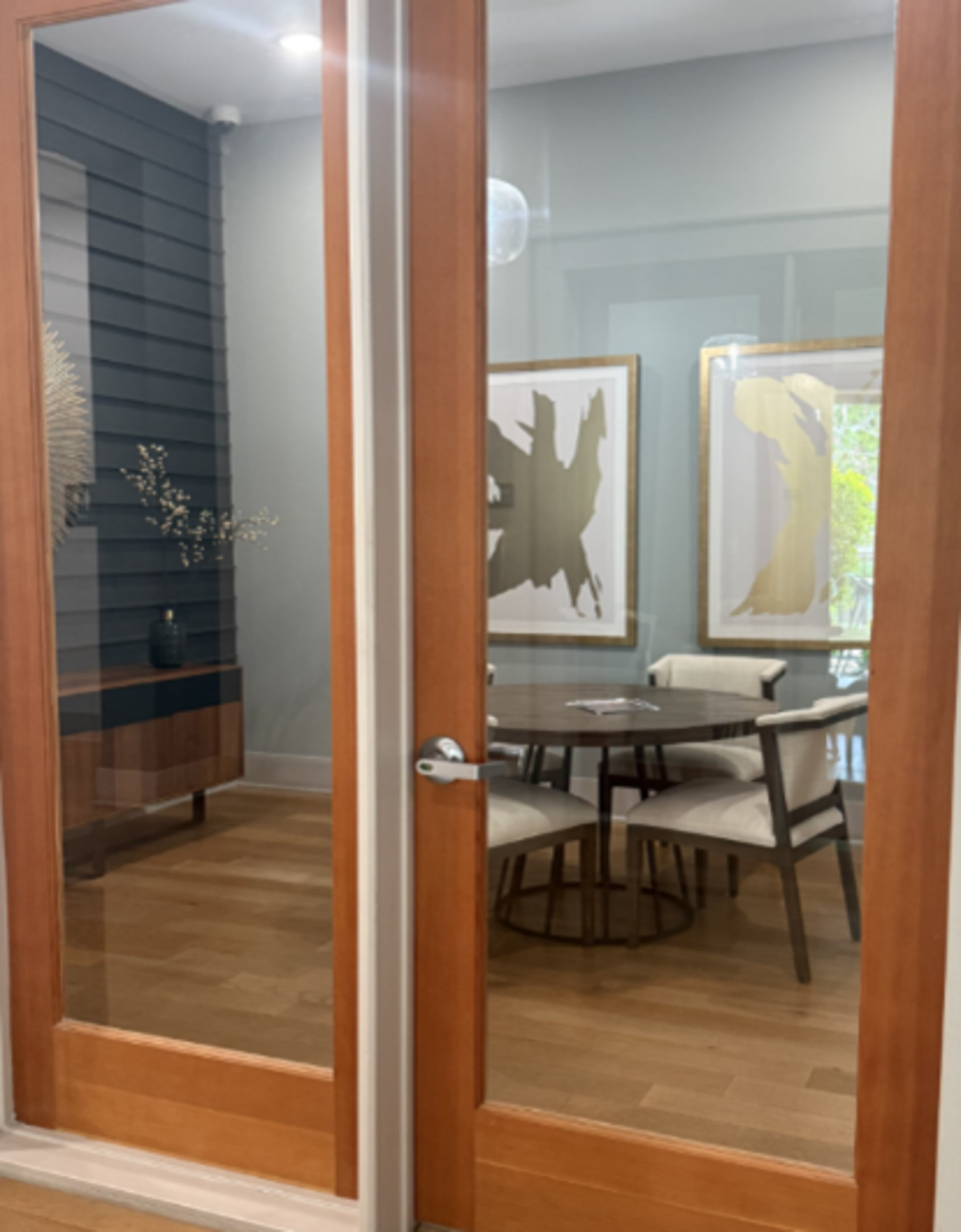 A glass door separates a modern room featuring a round table and abstract artwork on the walls.