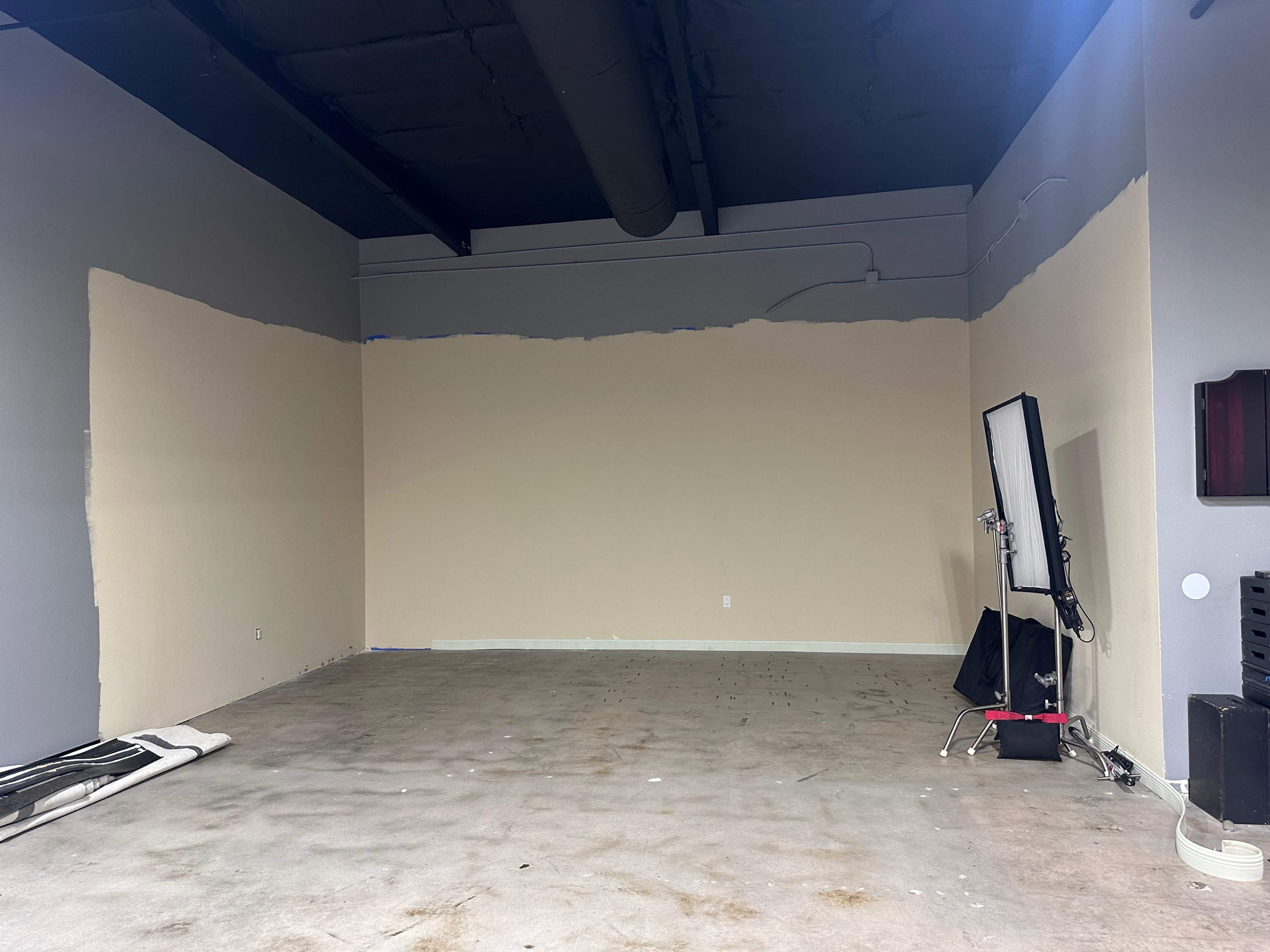 An unfinished interior space with one wall partially painted beige and a mirror on a stand in the corner.
