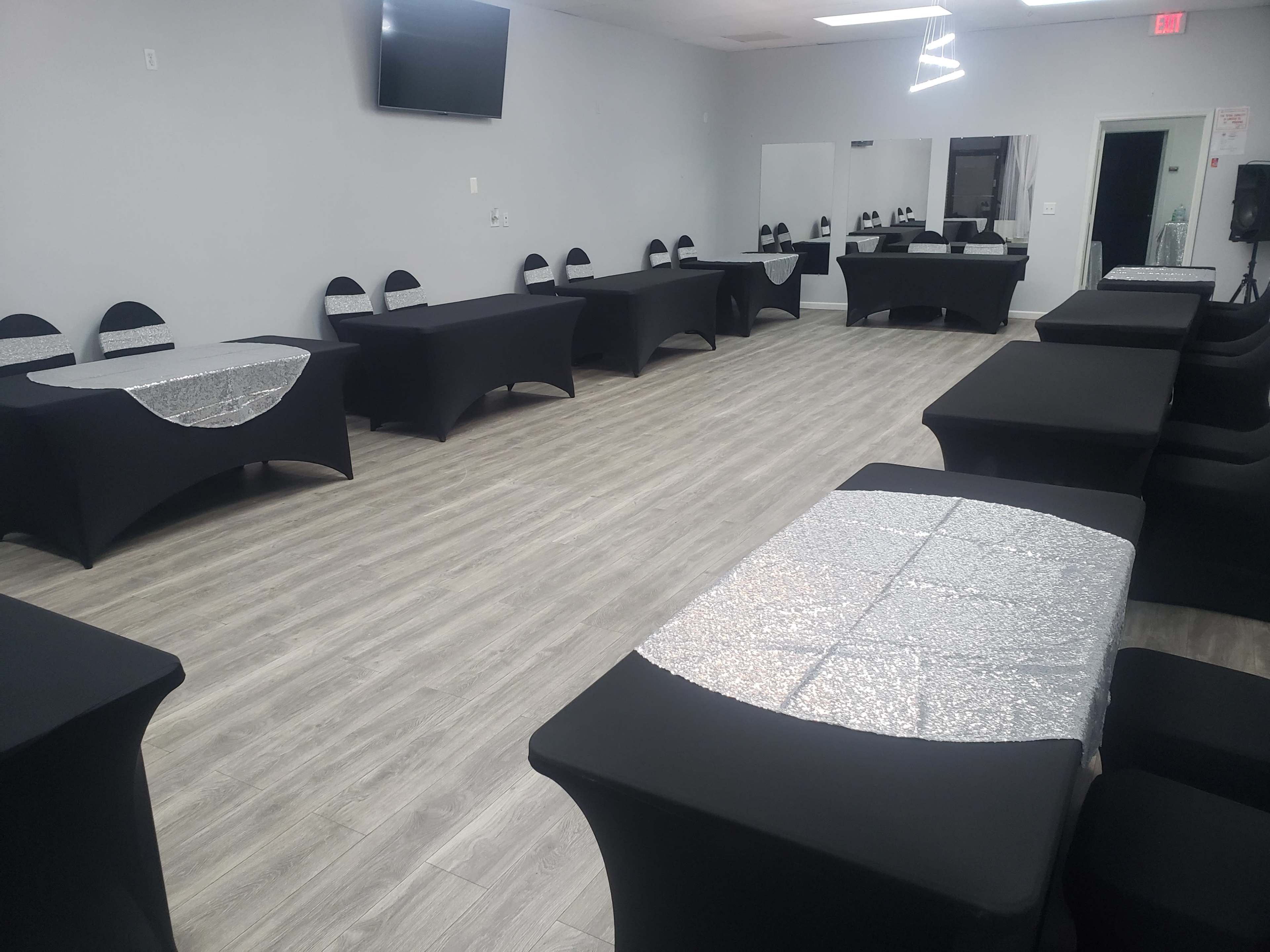 A spacious event room featuring several tables covered with black and silver tablecloths arranged in a neat layout.