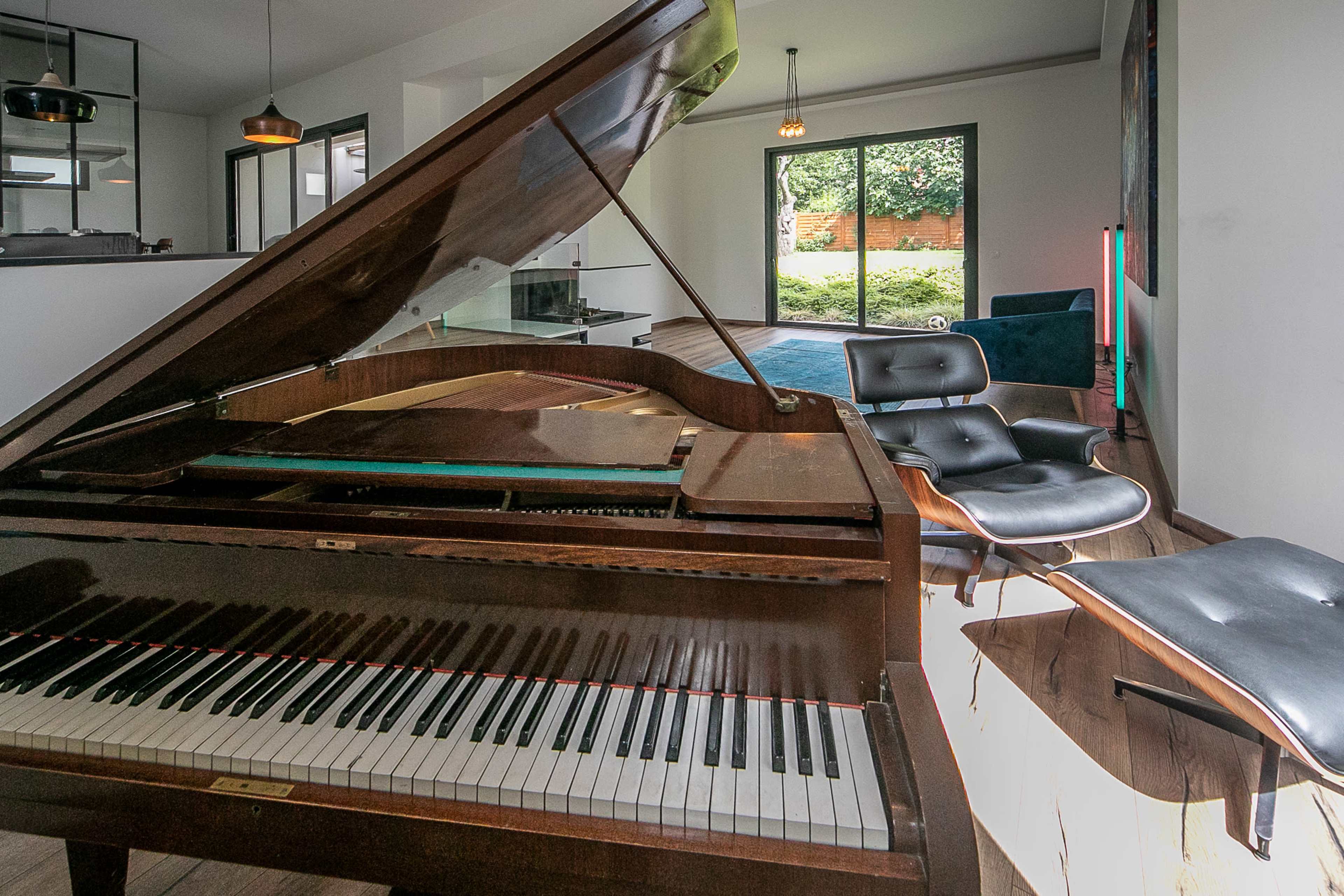 A grand piano is positioned in a modern living room, facing large glass doors that open to a landscaped backyard.