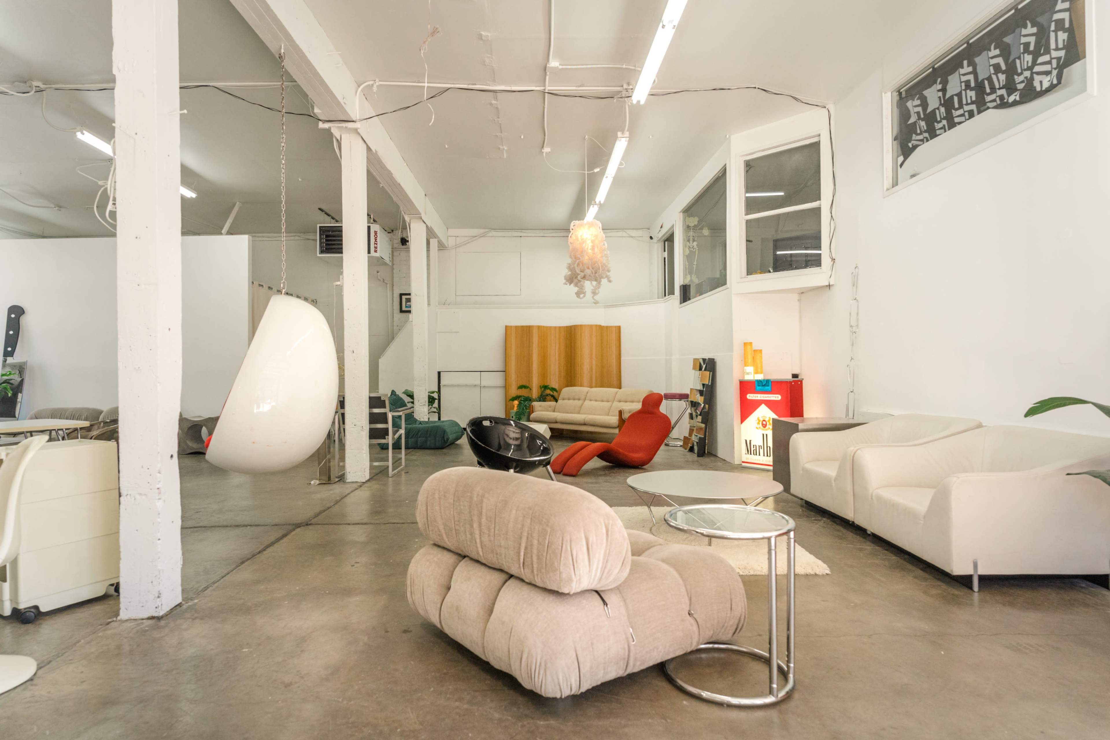 A spacious modern interior featuring various seating arrangements, including a hanging chair and multiple couches, with a minimalist decor in a well-lit environment.