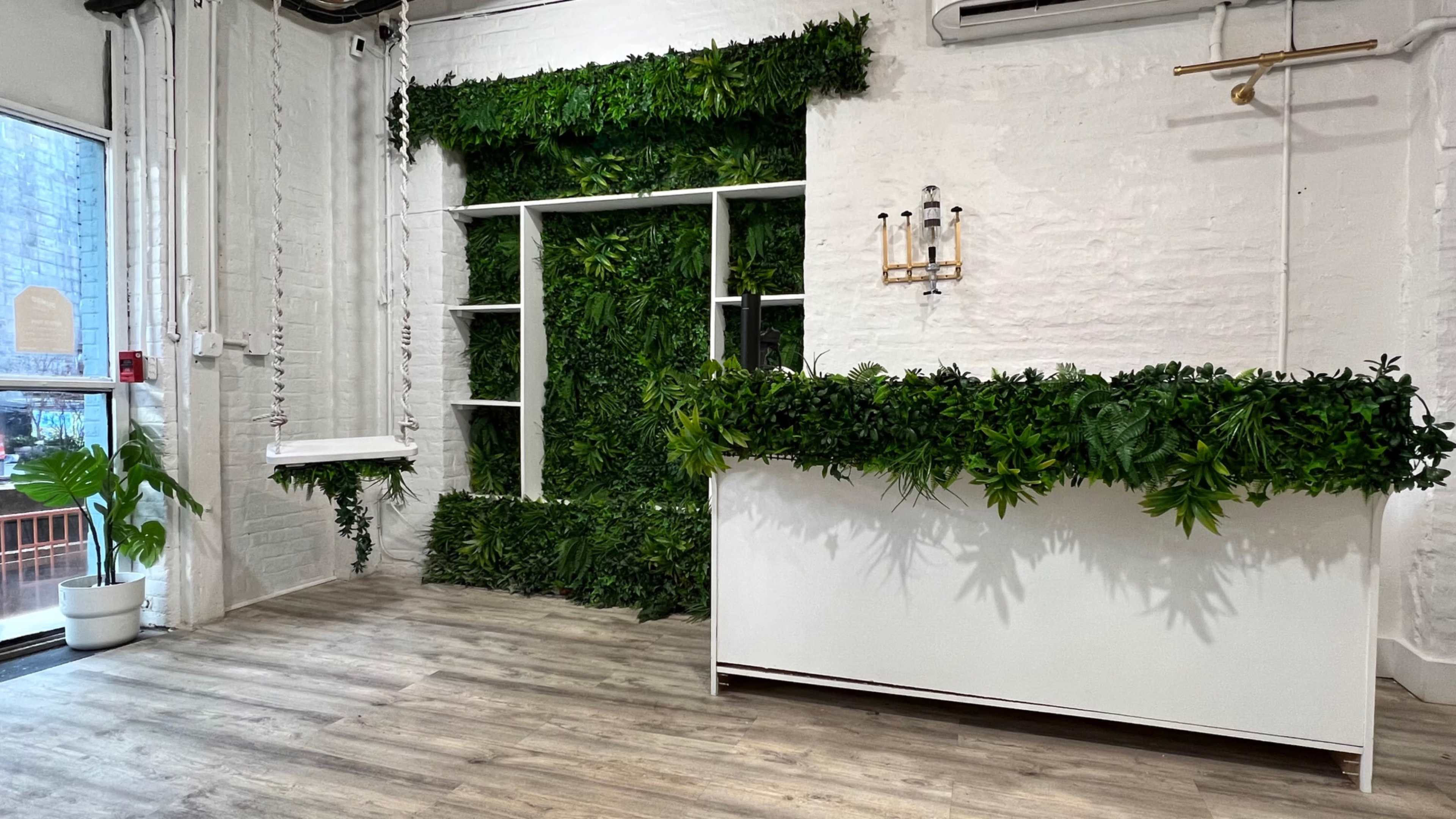 A modern reception area with a white desk and a wall covered in artificial greenery.