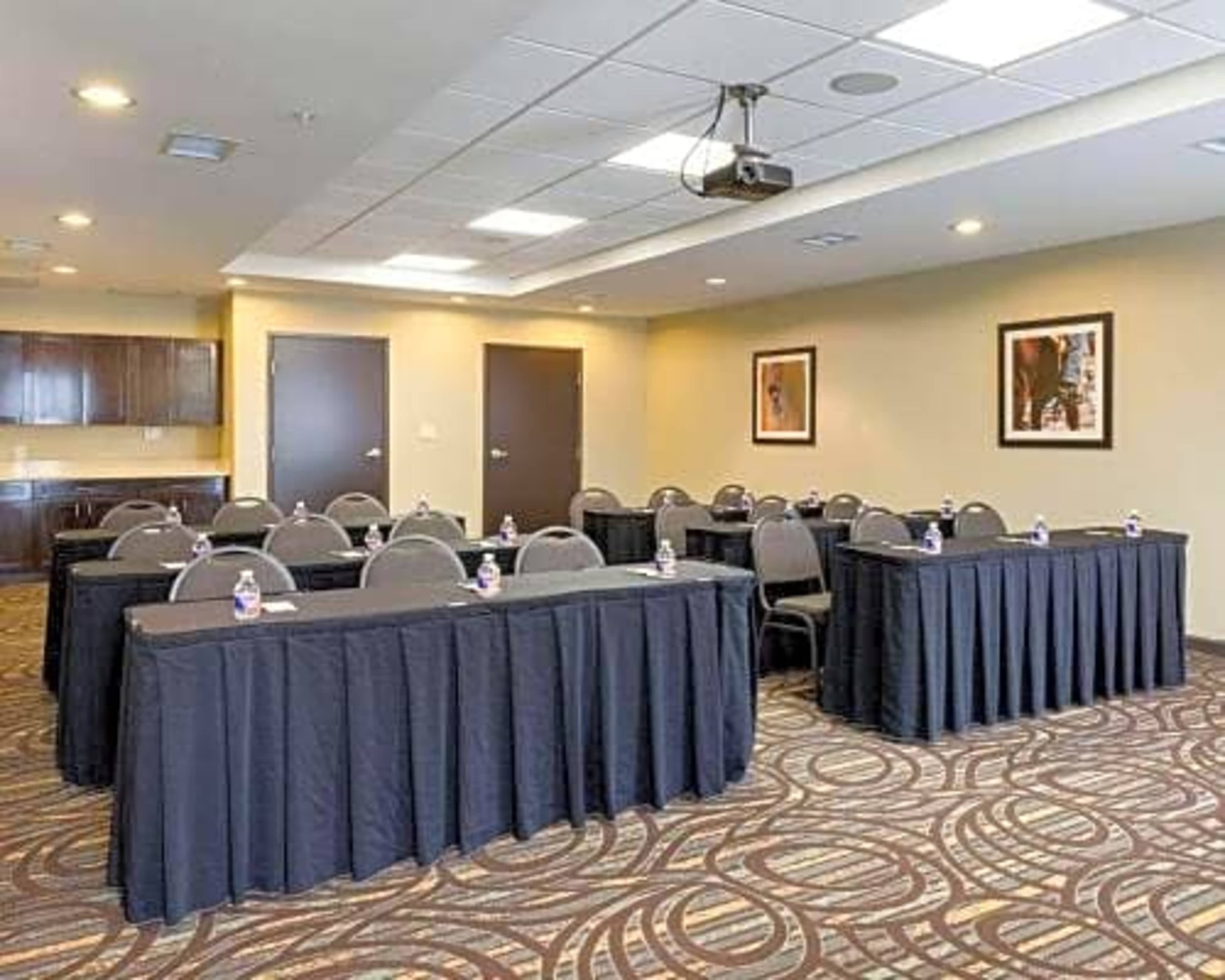 A conference room is set up with rows of tables covered in black cloth, each containing a water bottle, and a projector mounted on the ceiling.