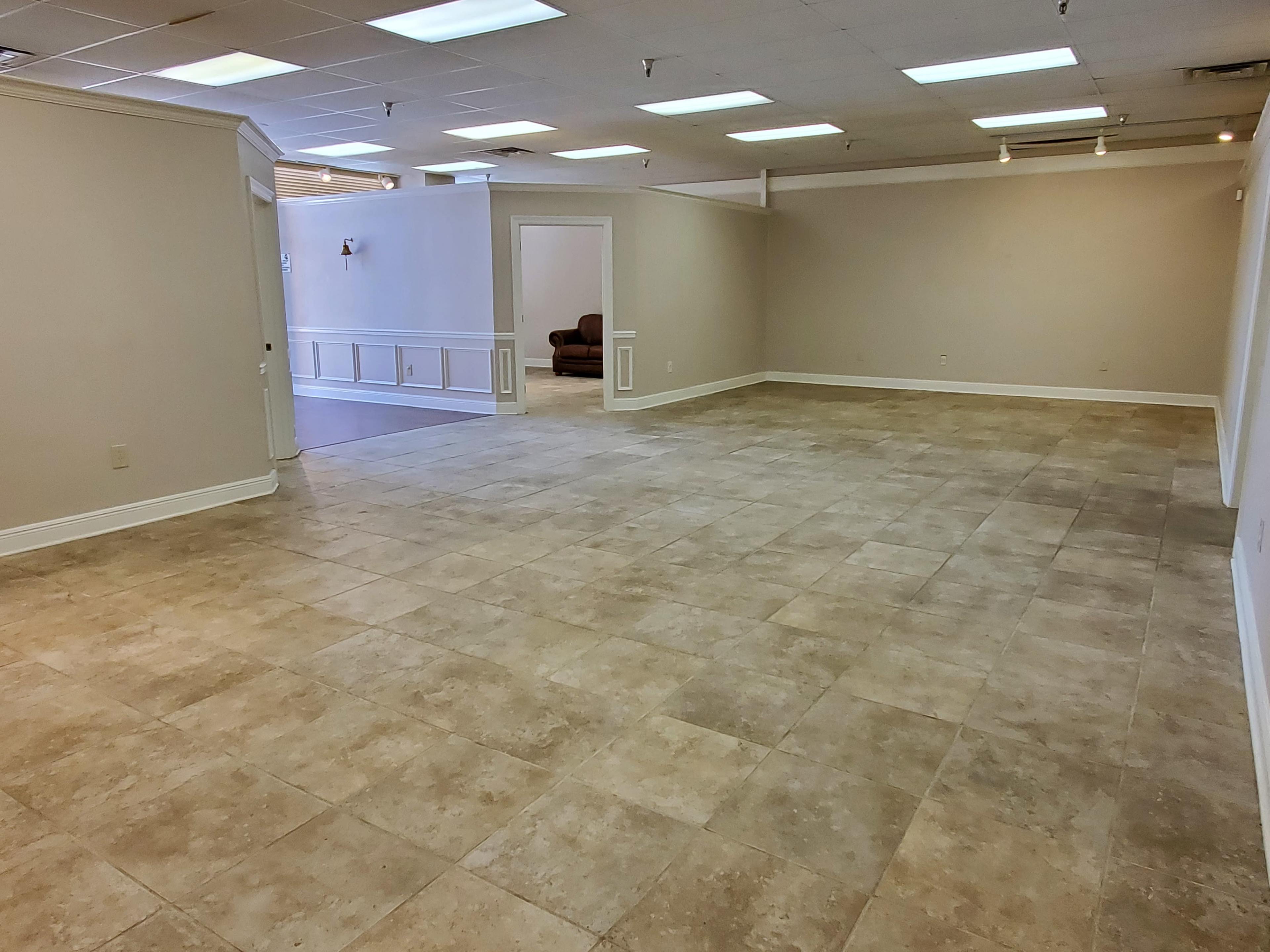 A spacious, empty room with tiled flooring and neutral-colored walls, illuminated by overhead lights.