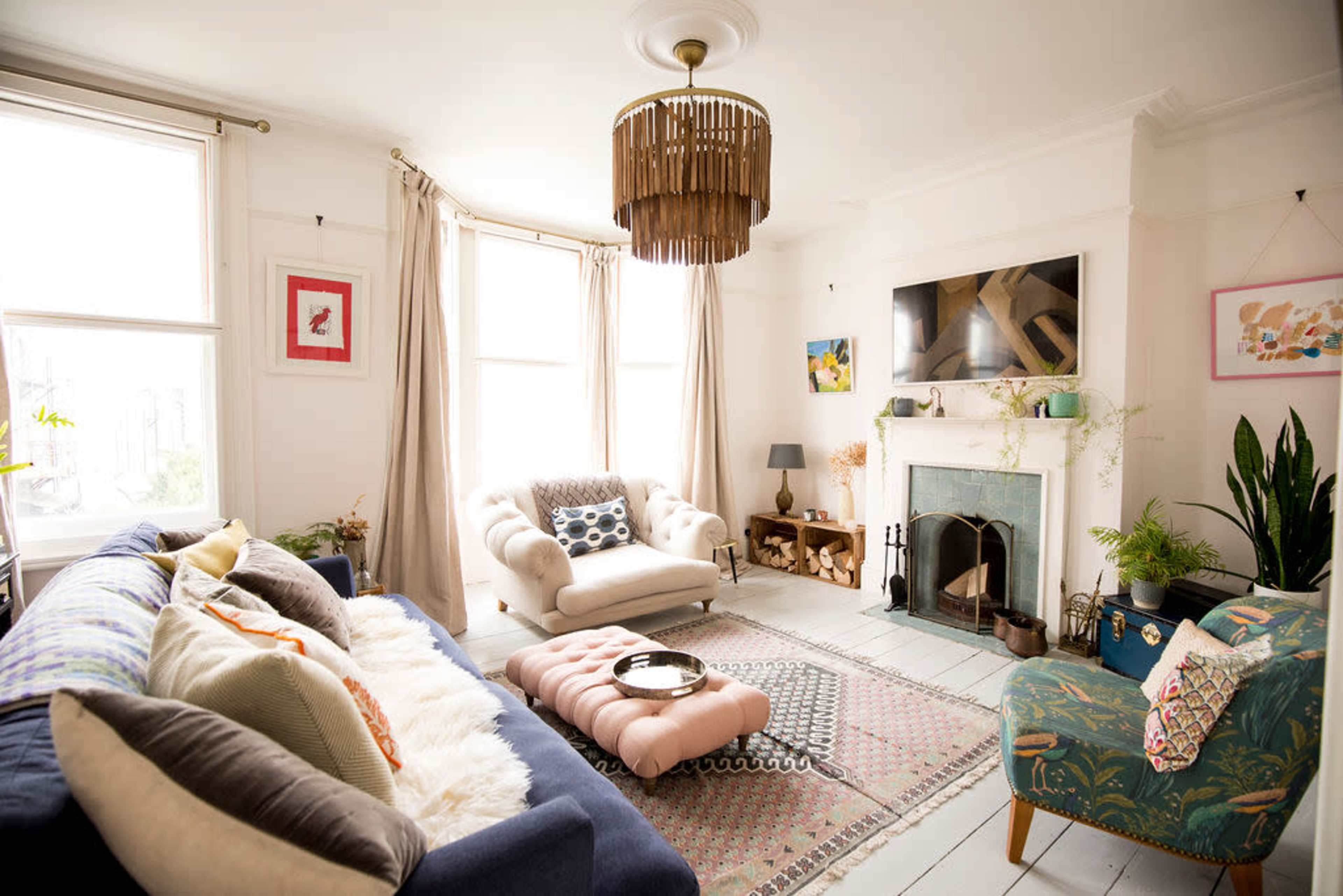 The image shows a well-lit living room featuring a blue sofa, a cream-colored armchair, a coffee table, and a fireplace with decorative items.