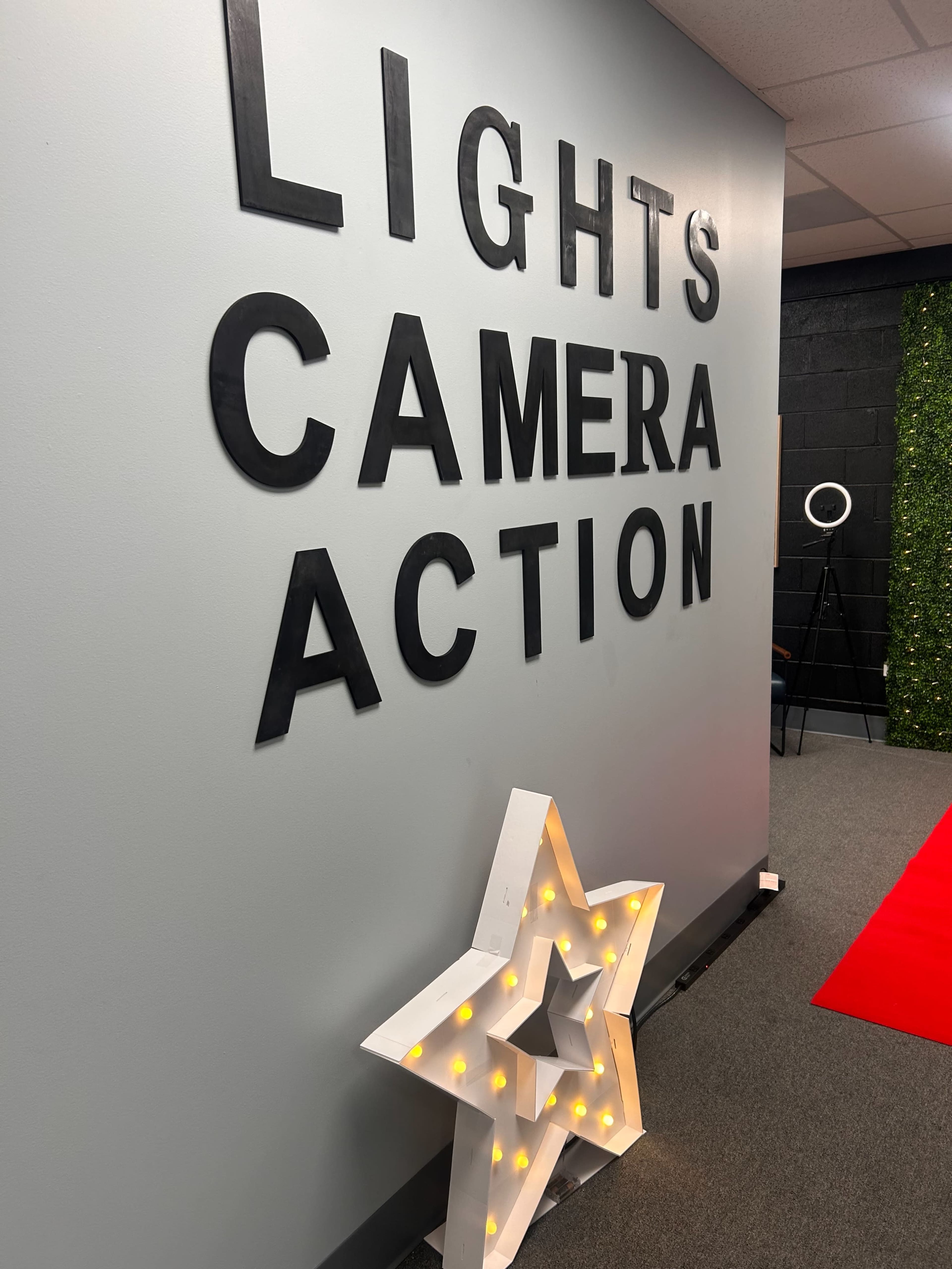 The image shows a wall with the words "LIGHTS CAMERA ACTION" displayed prominently above a white star-shaped decor with lights, set against a gray background.