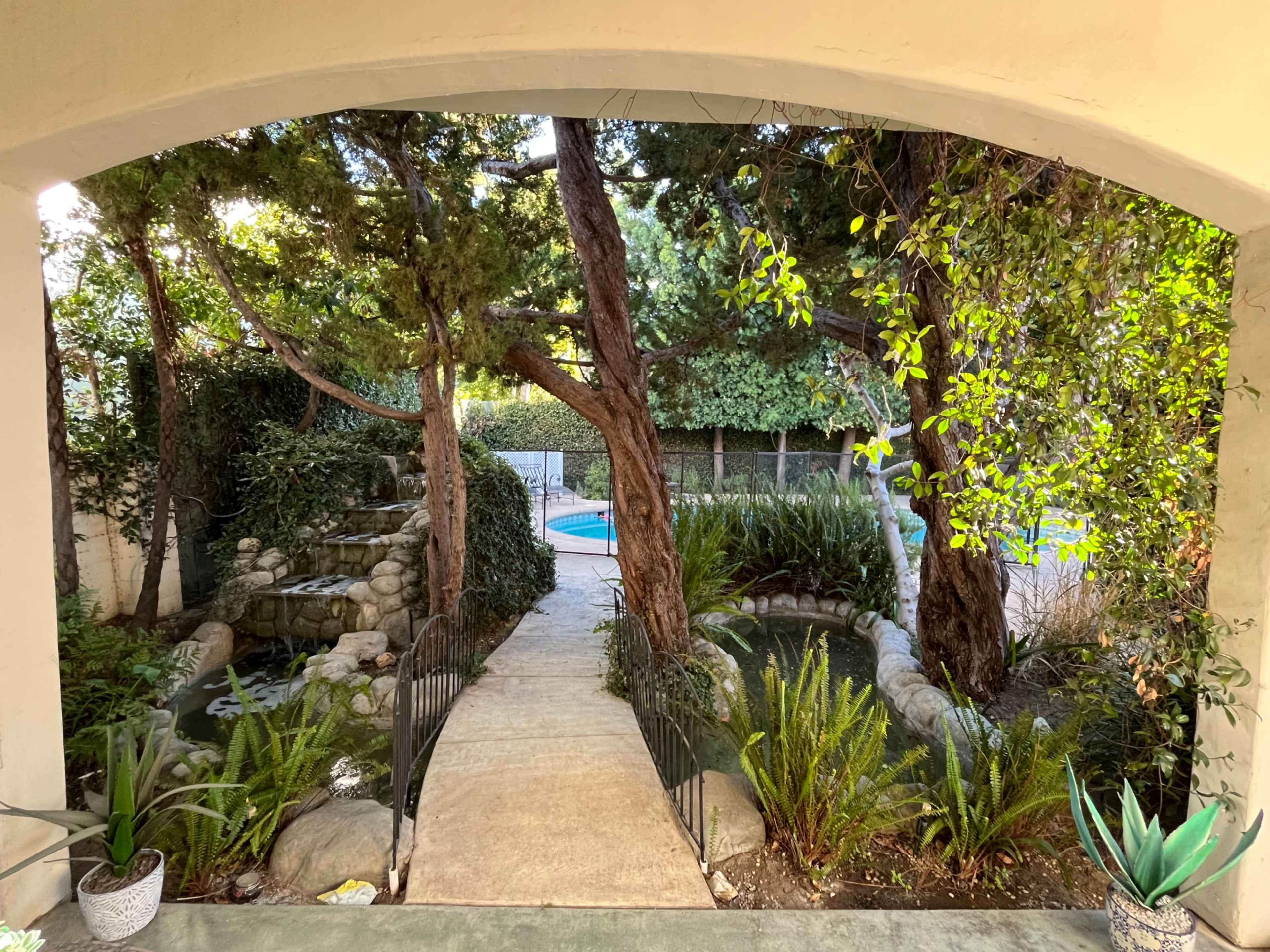 A stone pathway leads through lush greenery to a pool surrounded by trees and shrubs.