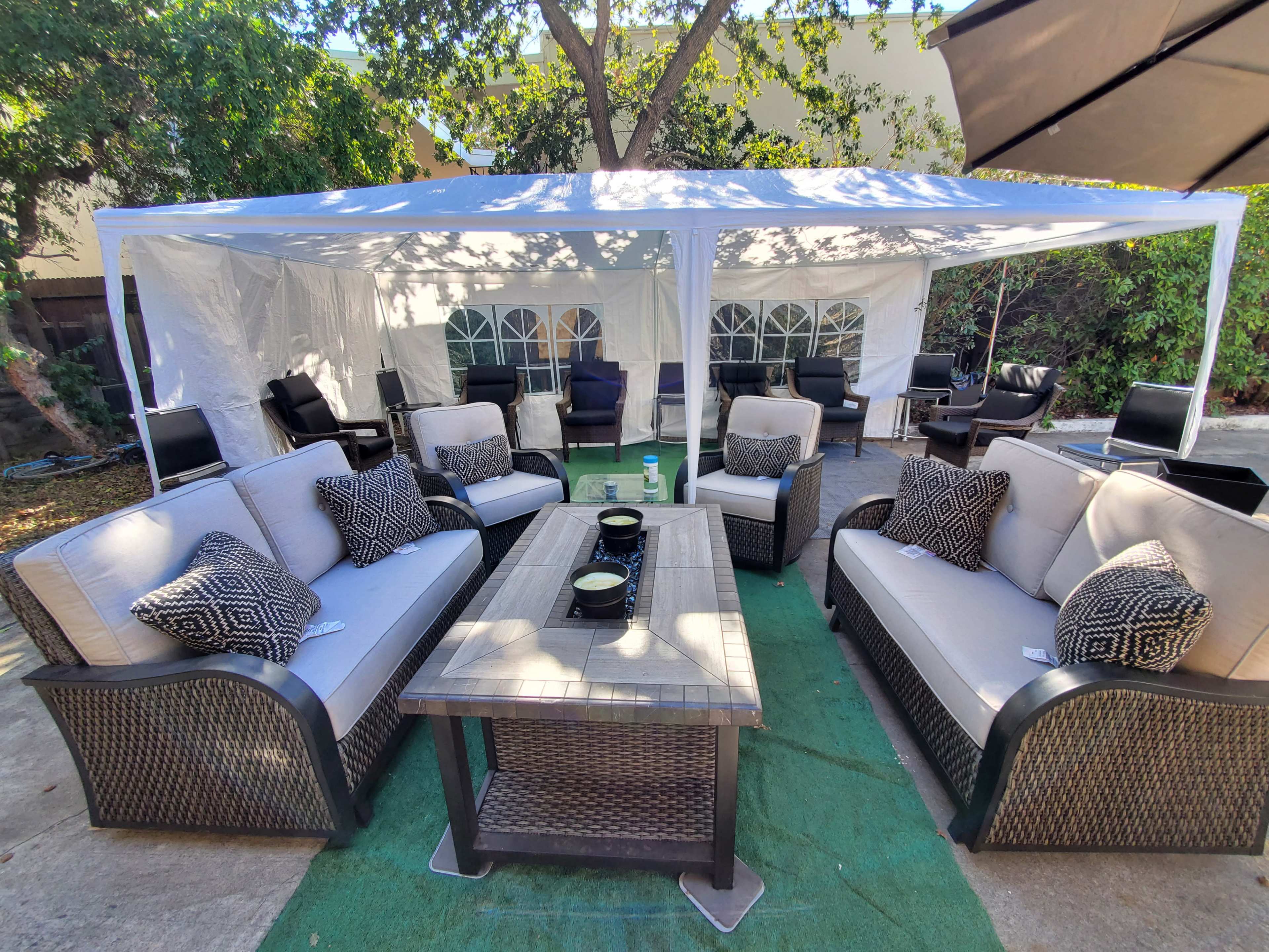 A spacious outdoor seating area features two sets of sofas and a coffee table under a white tent surrounded by chairs.