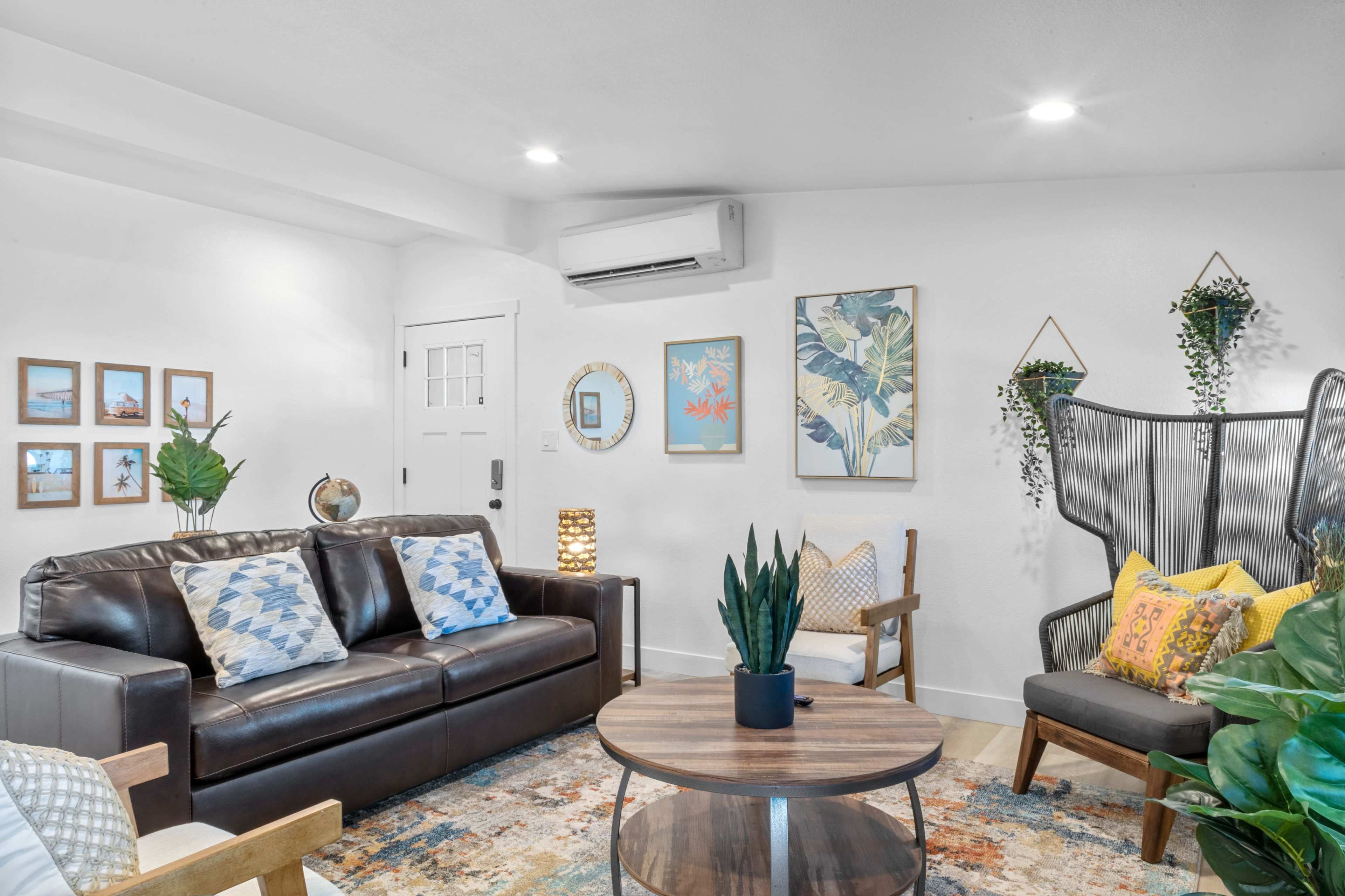A cozy living room features a leather sofa, decorative plants, and framed artwork on the walls, with a round coffee table in the center.