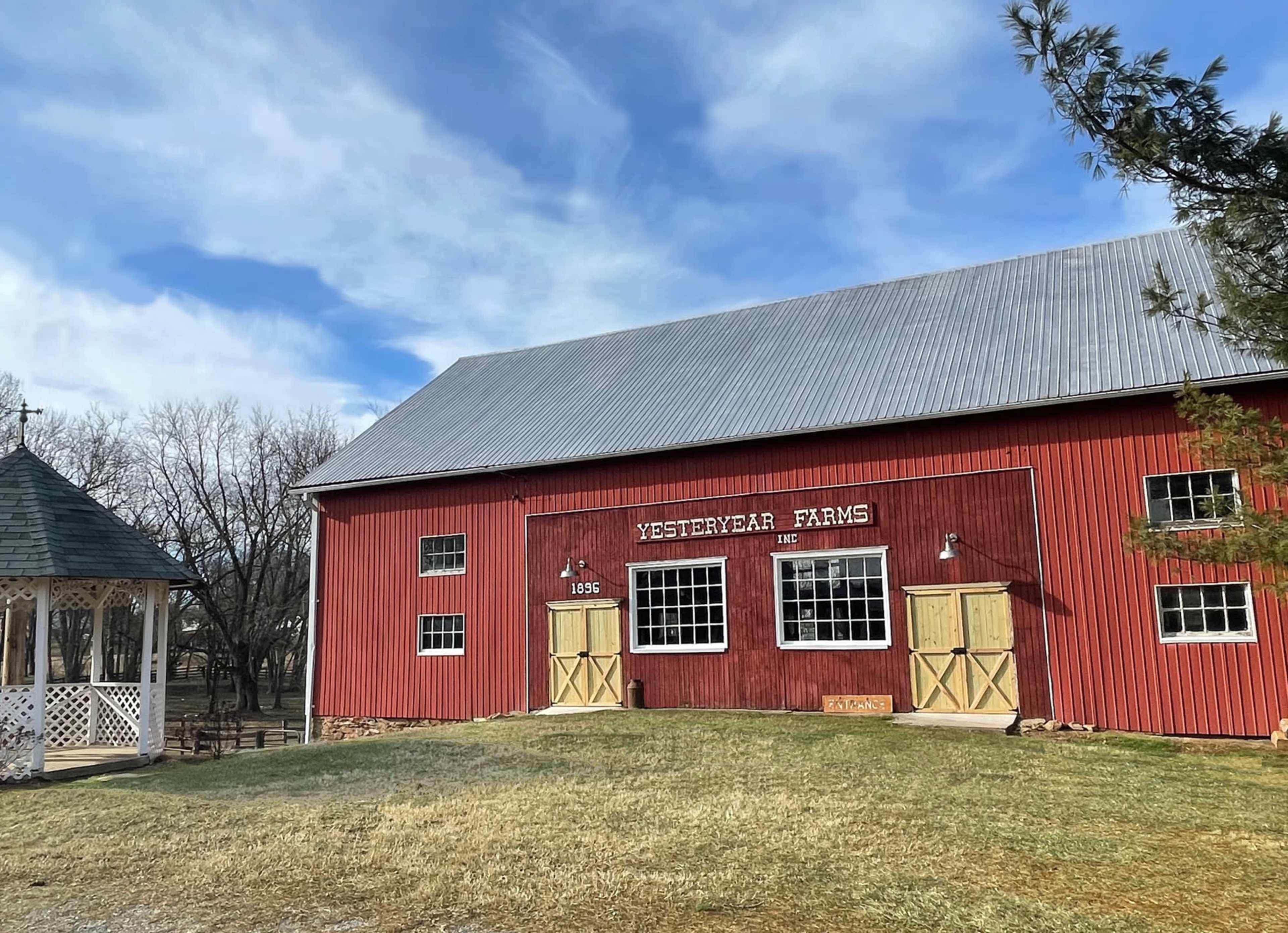 A red barn labeled "Yesteryear Farms" with wooden doors, situated on a grassy area under a partly cloudy sky.