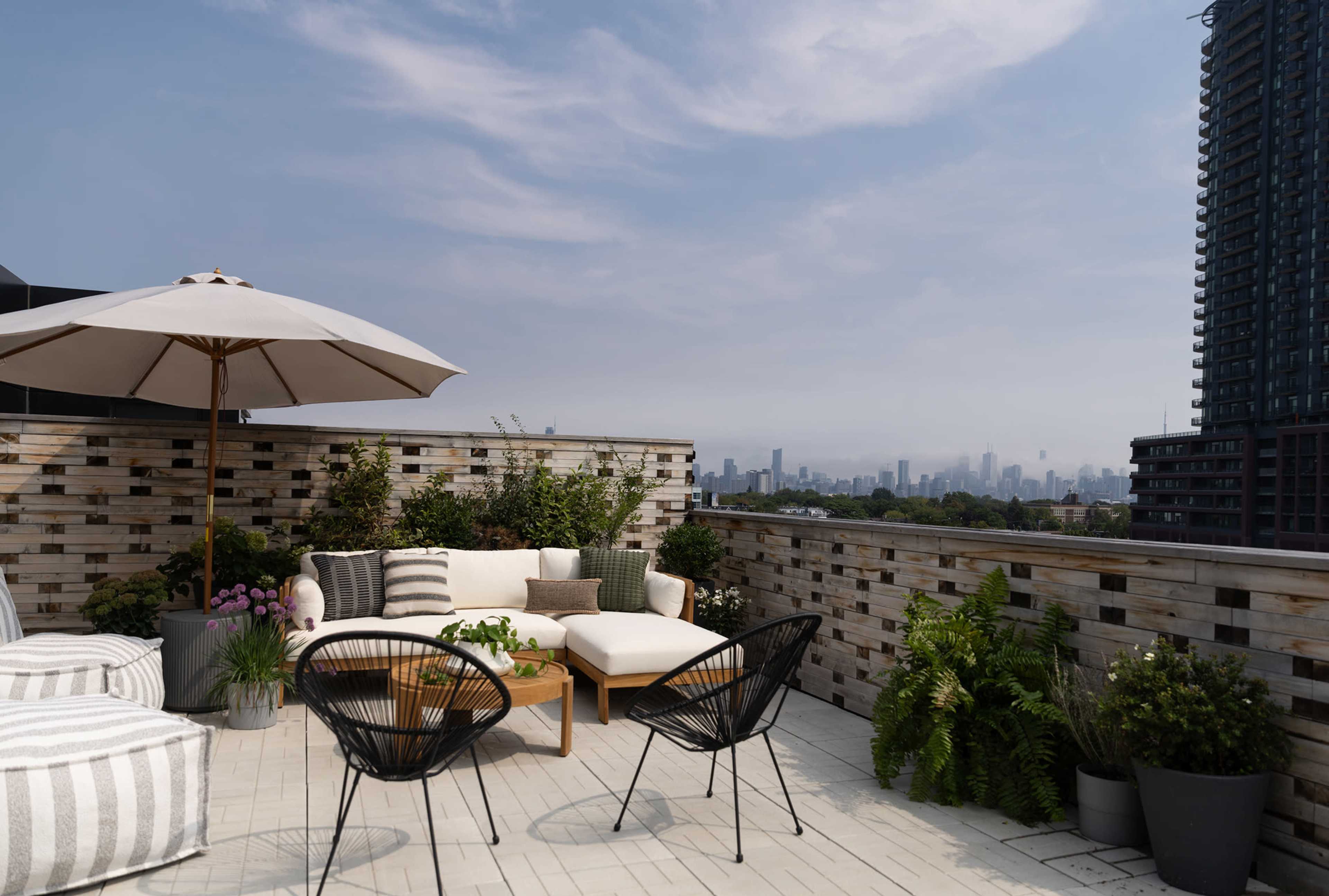 The image depicts a modern rooftop terrace with a seating area, an umbrella, and city views in the background.