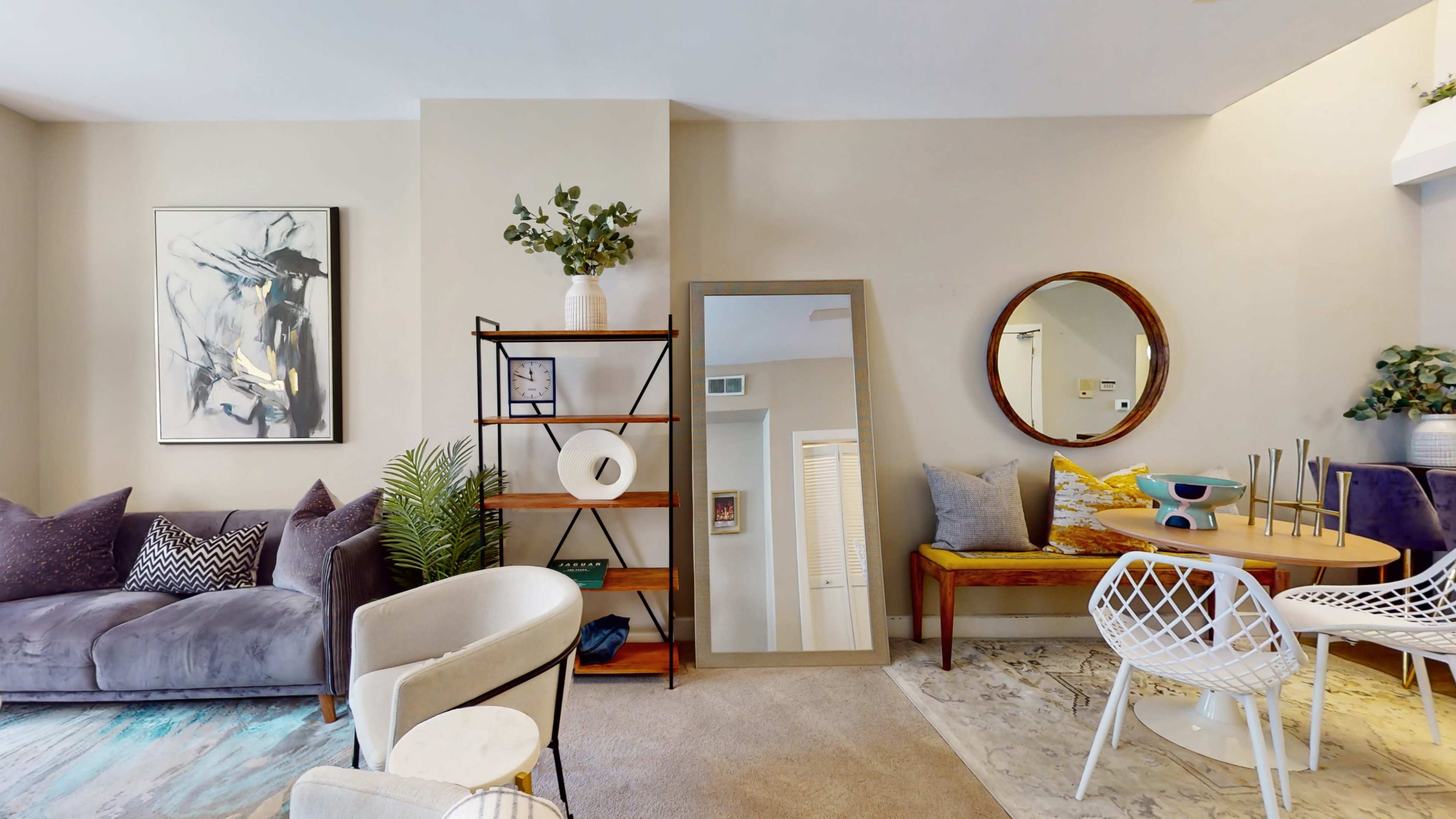 A living room features a cozy seating area with a large mirror, decorative plants, and a round dining table surrounded by chairs.