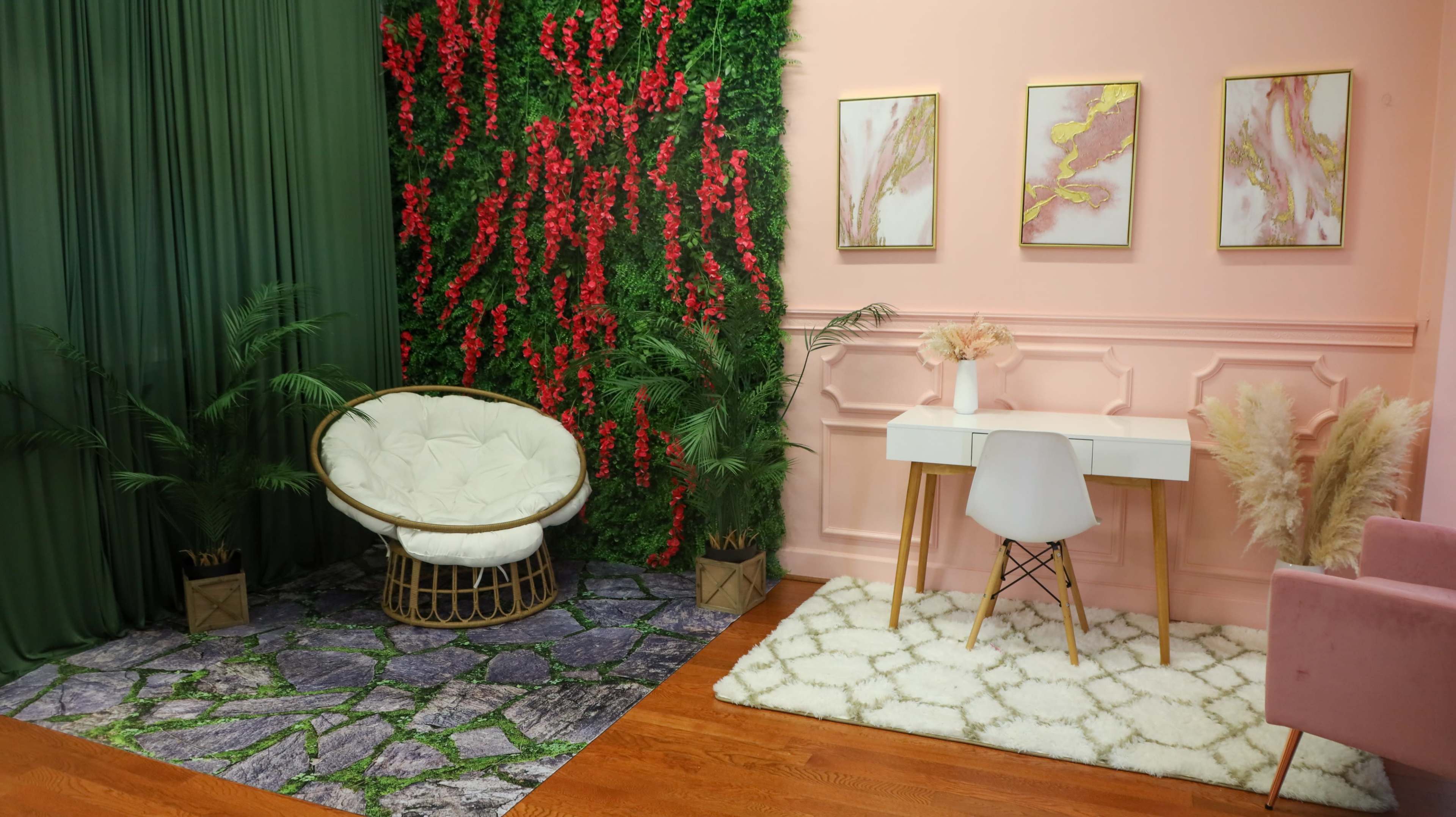 A stylish indoor space with a green wall featuring red foliage, a white cushioned chair, a minimalist desk, and decorative art on the pink wall.