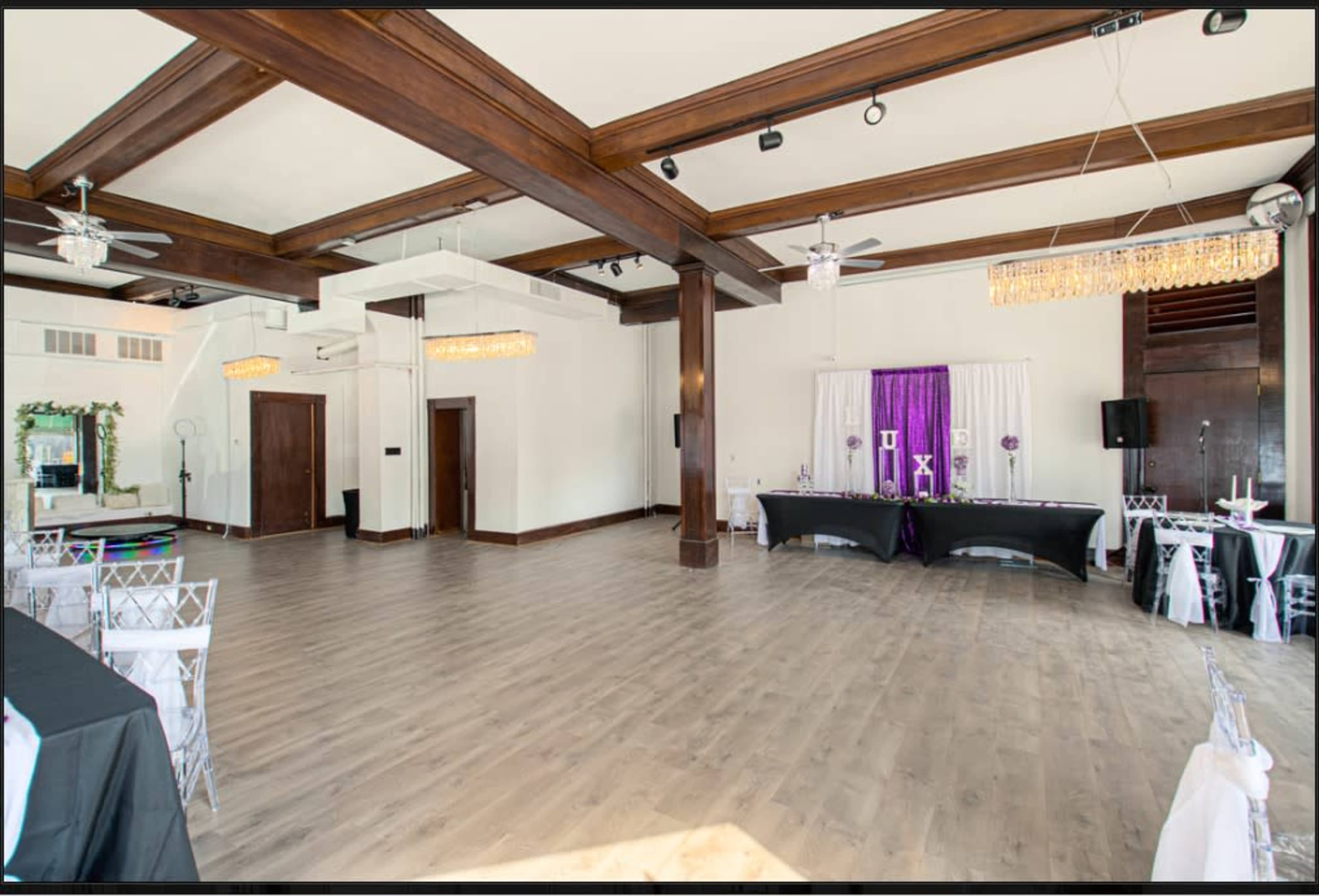 A spacious event hall featuring wooden beams, modern lighting, and tables set up along the sides.