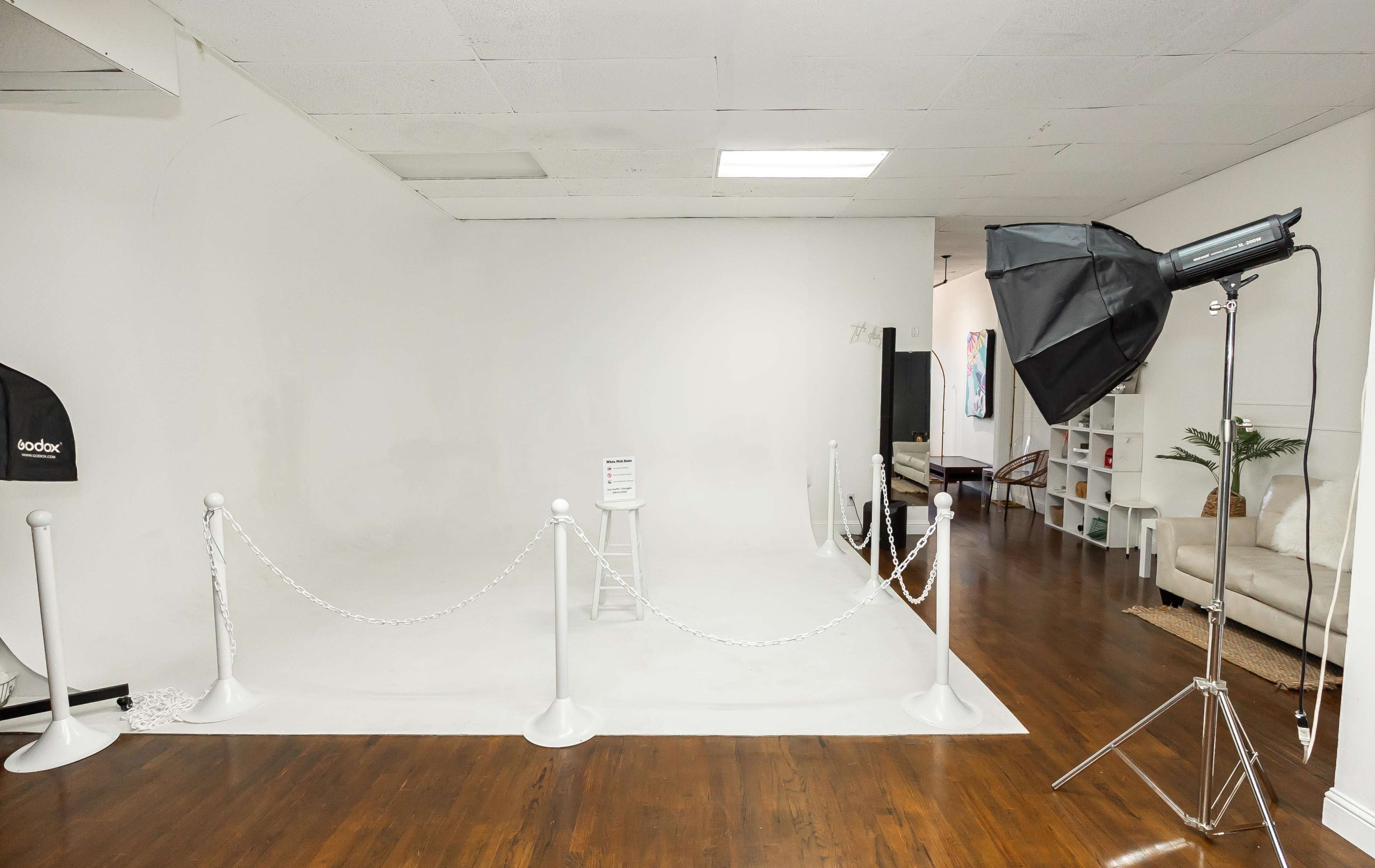A photo studio with a plain white backdrop, a stool, and a lighting setup is visible, surrounded by a rope barrier.