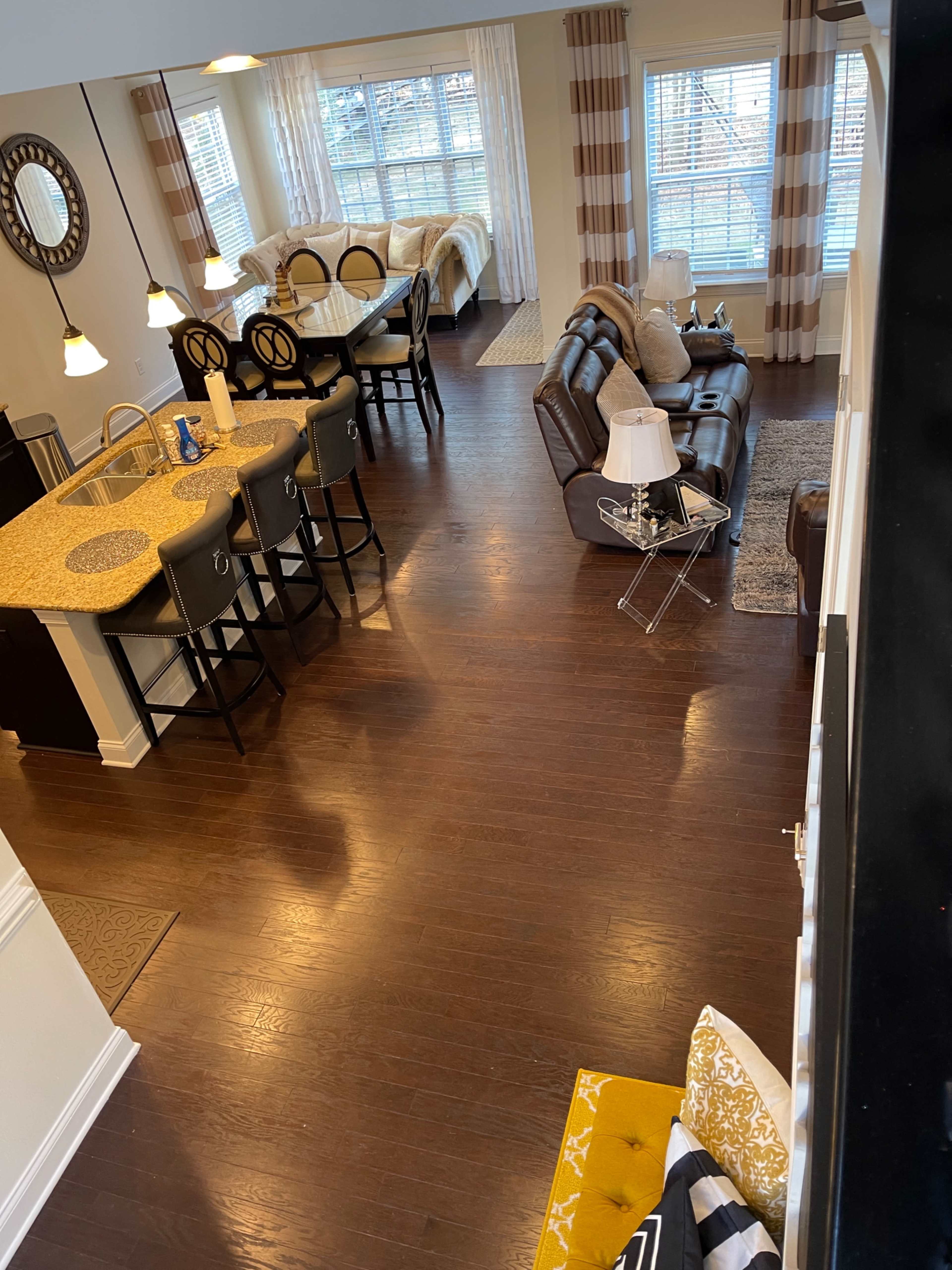 A spacious living area with a dining table, chairs, and a sofa set, featuring large windows that allow natural light to enter the room.