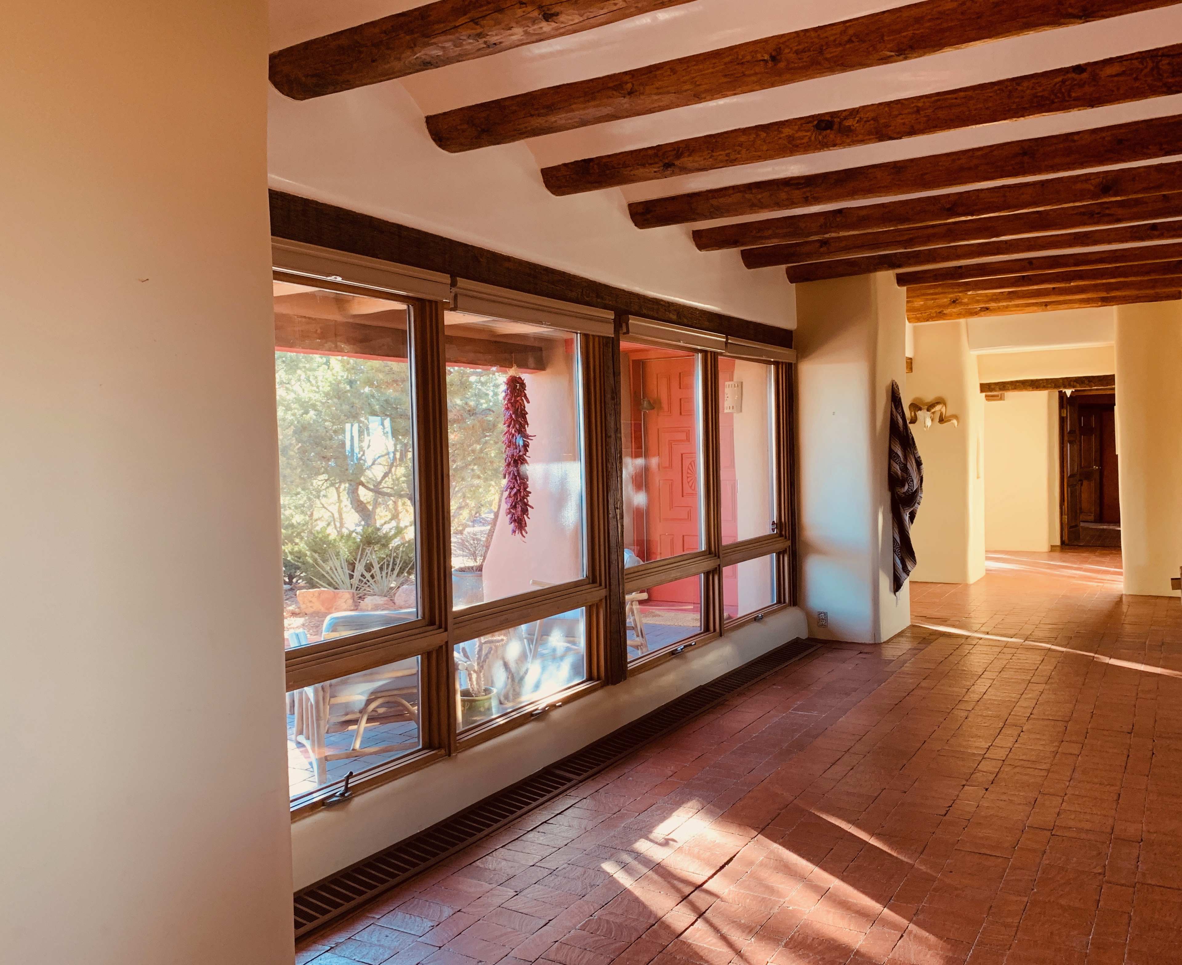 A hallway with wooden beams on the ceiling, large windows on one side, and a terracotta tile floor.