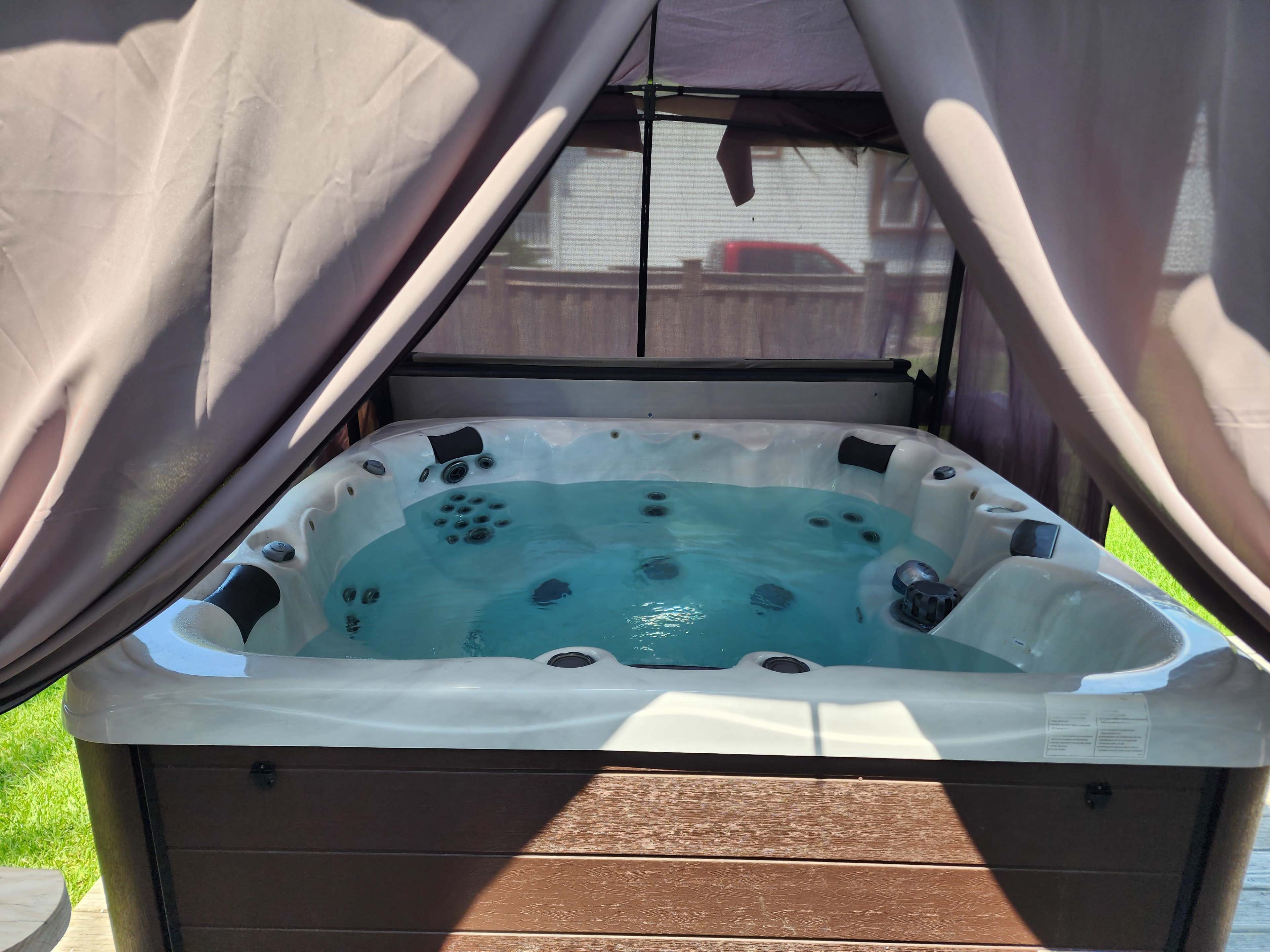 A hot tub filled with water is positioned under a canopy on a wooden deck.