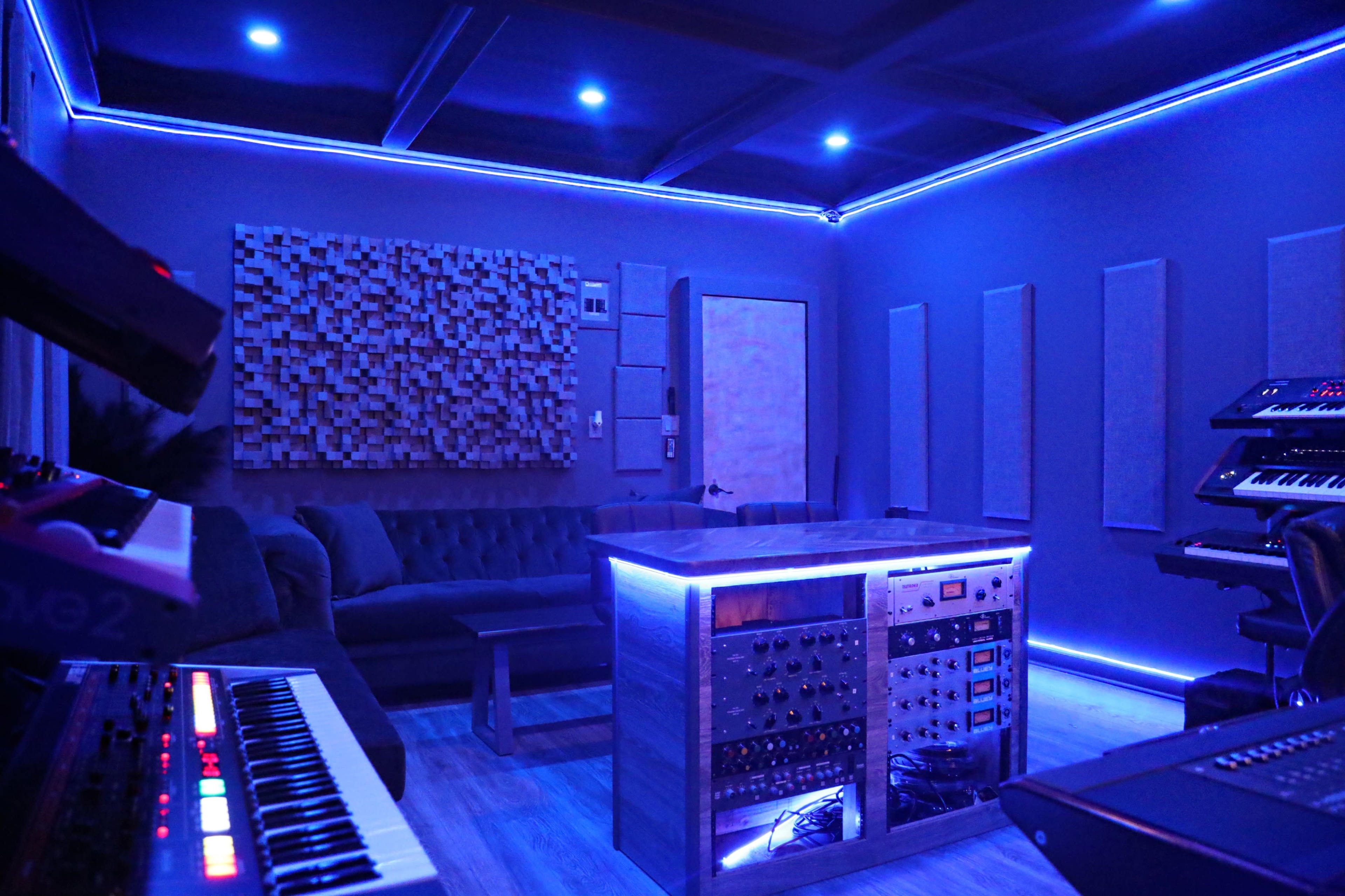 A music studio with a couch, a mixing desk surrounded by equipment, and blue LED lighting installed along the perimeter.
