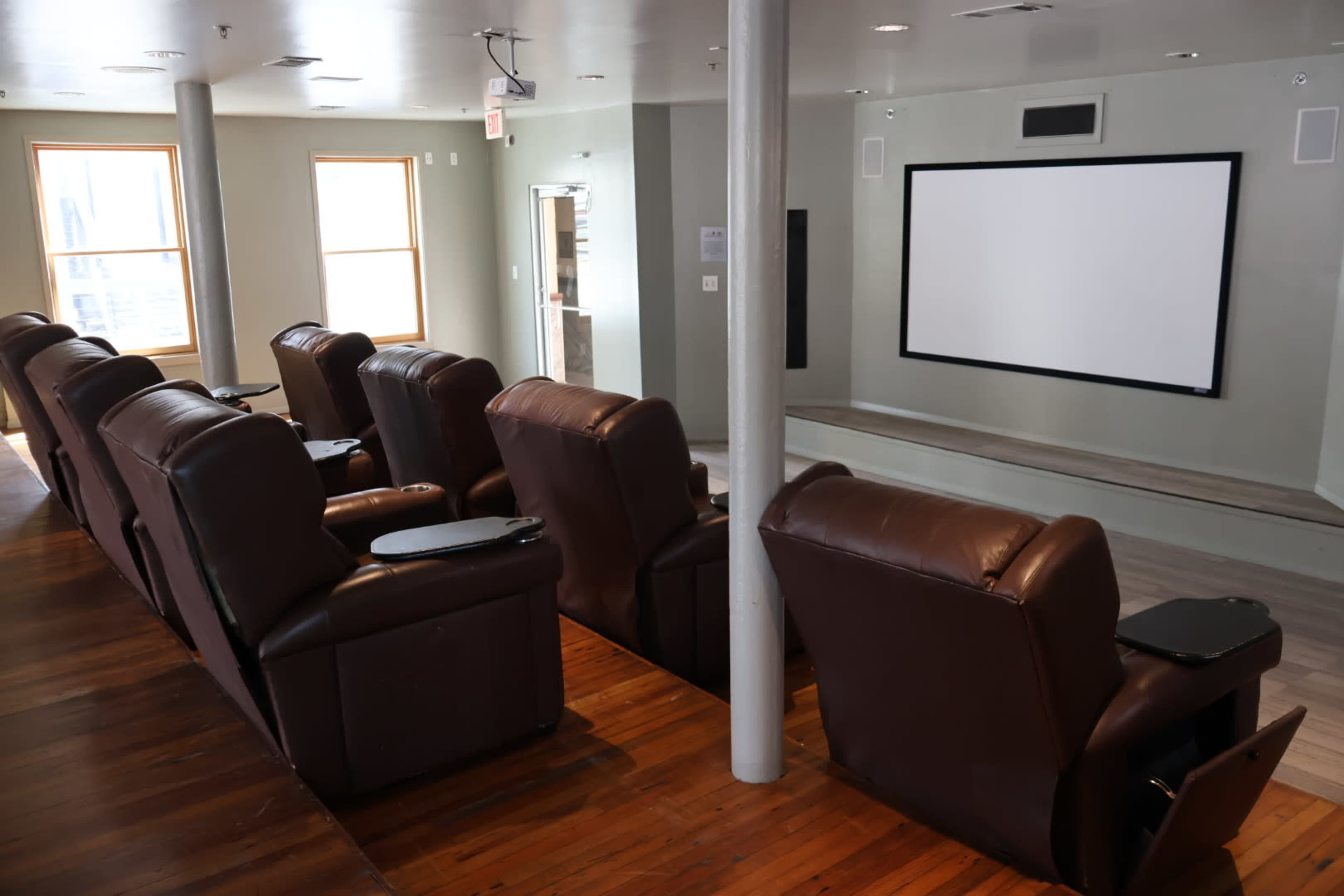 The image shows a home theater setup with brown reclining chairs arranged in front of a large blank screen on the wall.