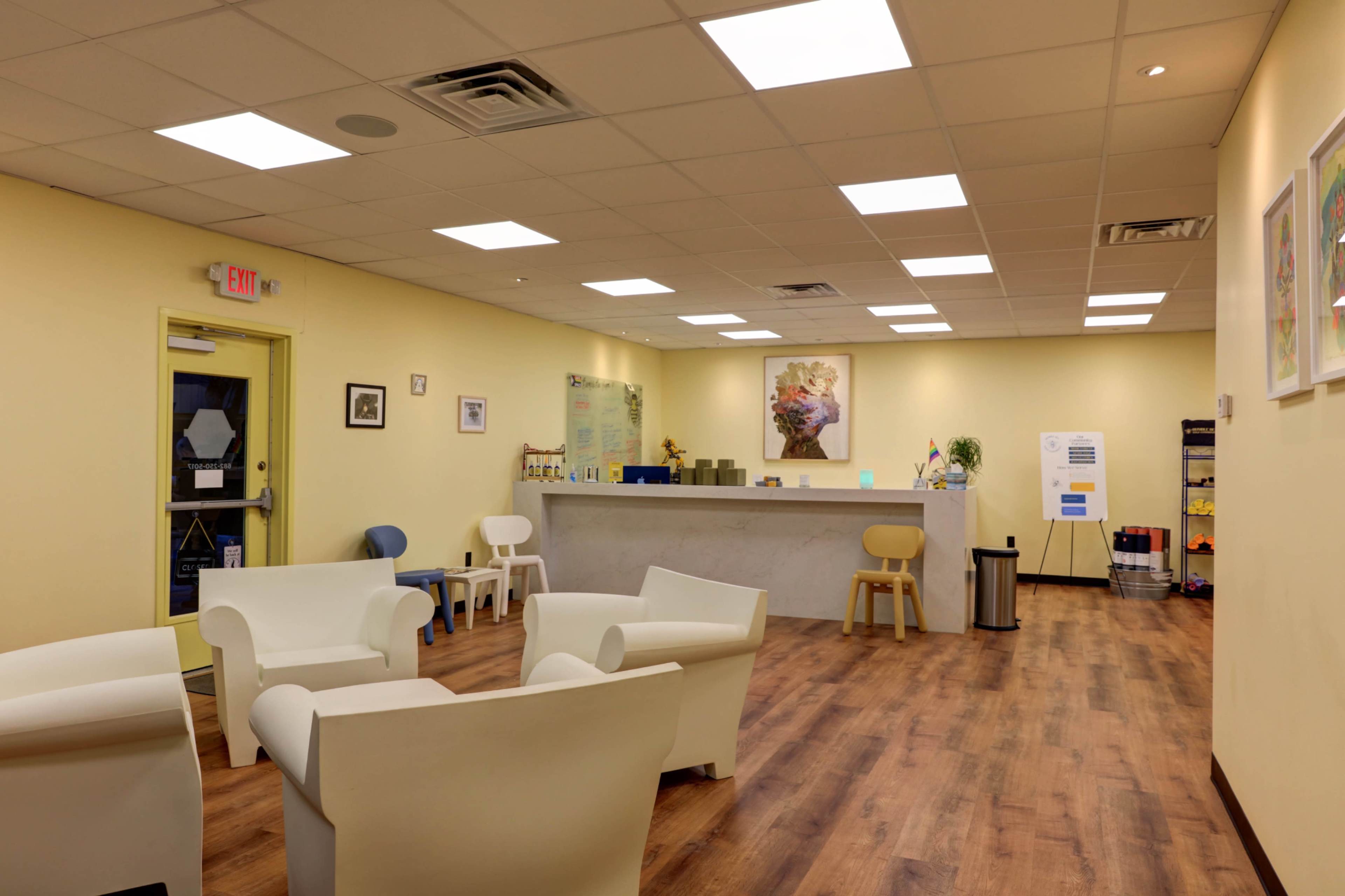 A bright, modern waiting area with light yellow walls, a reception counter, and several white chairs arranged around the space.