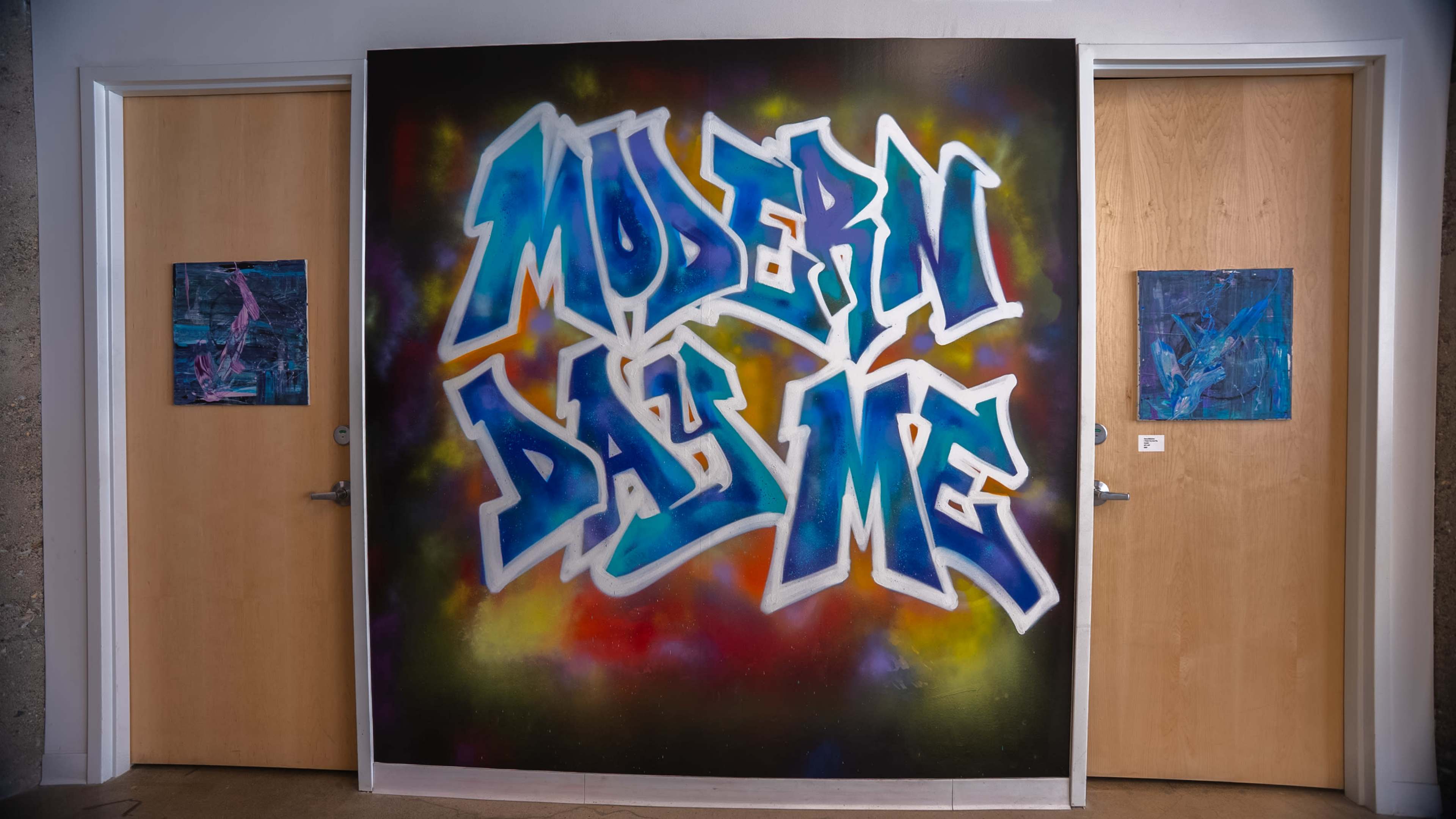 The image features a large graffiti mural with the words "MODERN DAY ME" in bold blue and white letters on a colorful background, flanked by two doors at either side.