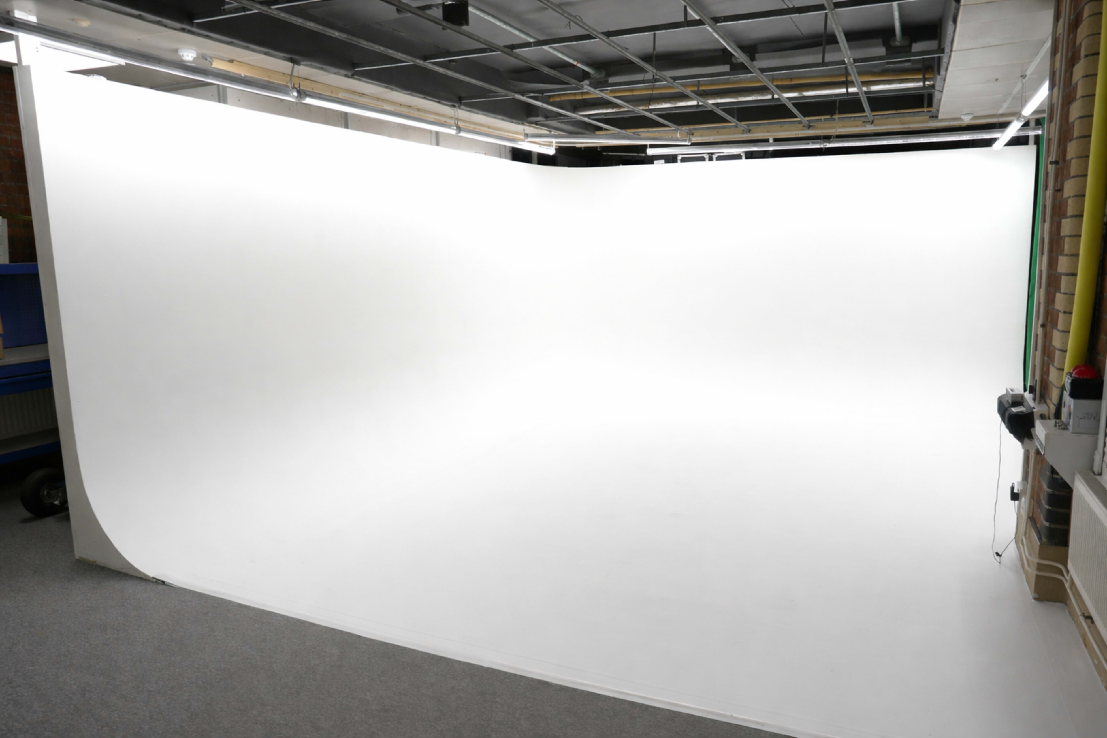 The image shows a large, empty photography studio with a seamless white backdrop and a flat floor.