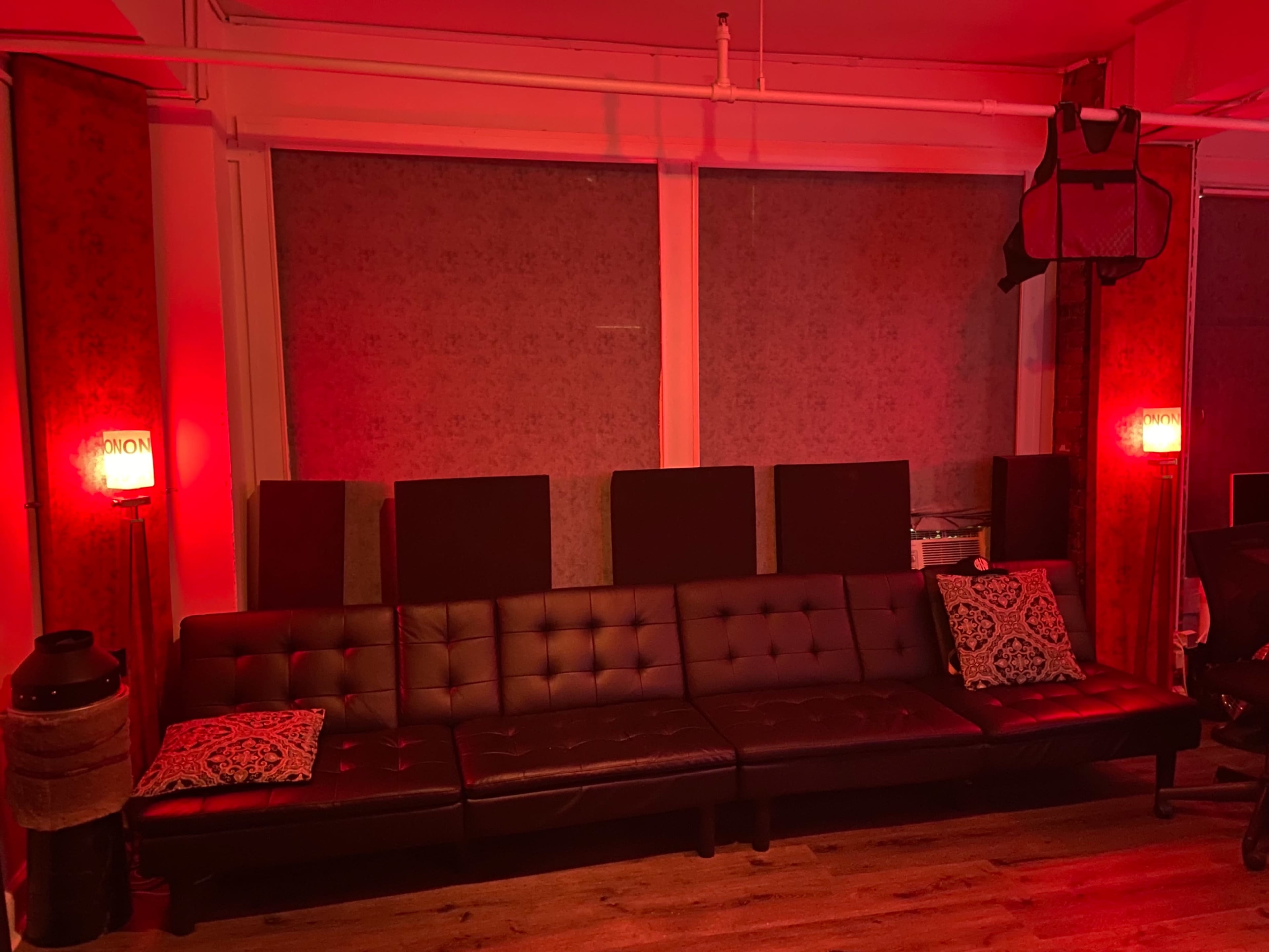 A dark room features a leather sectional sofa with decorative pillows, illuminated by red wall sconces.
