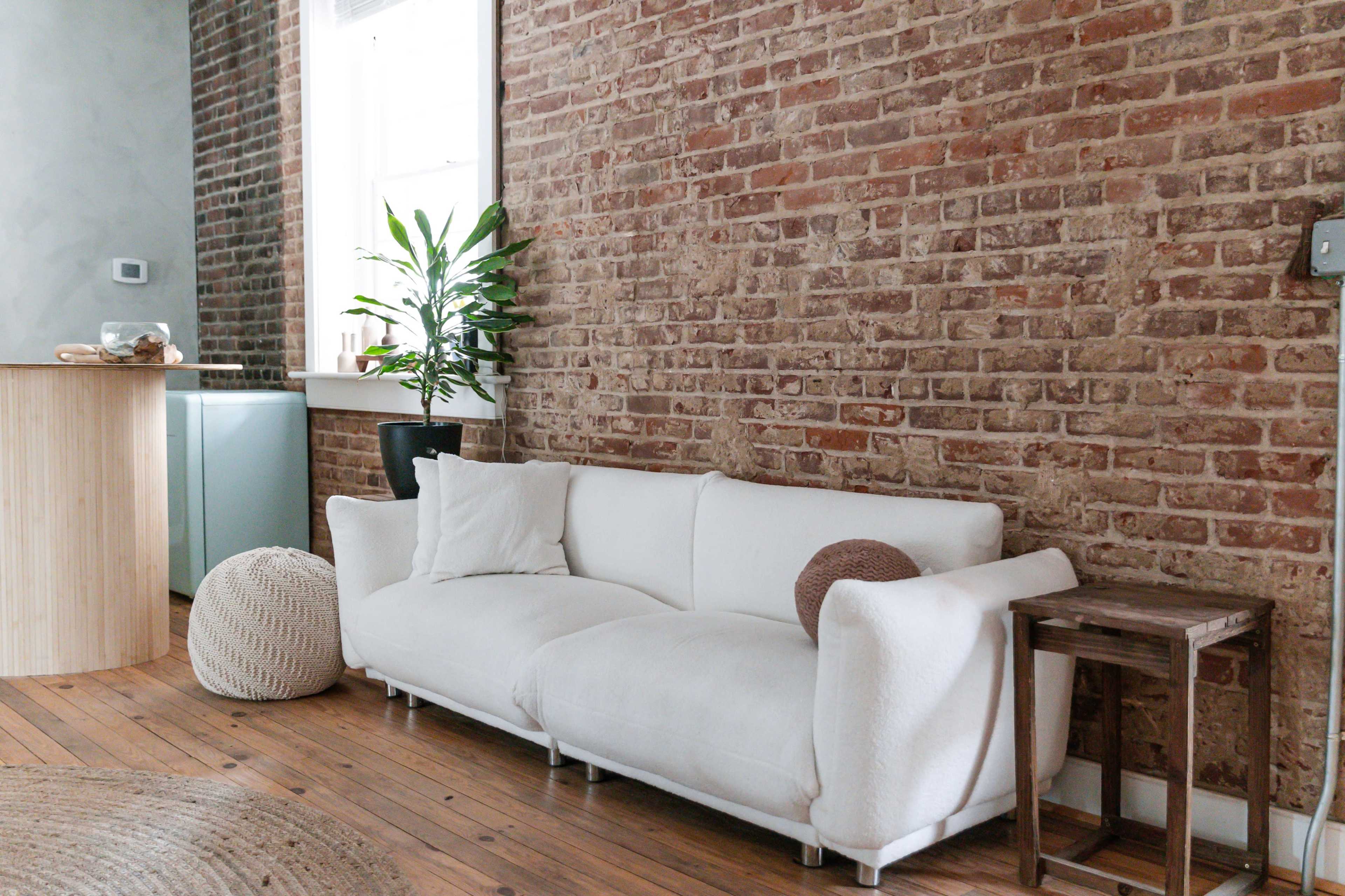 A white couch is positioned against a brick wall, alongside a small wooden table and a potted plant.