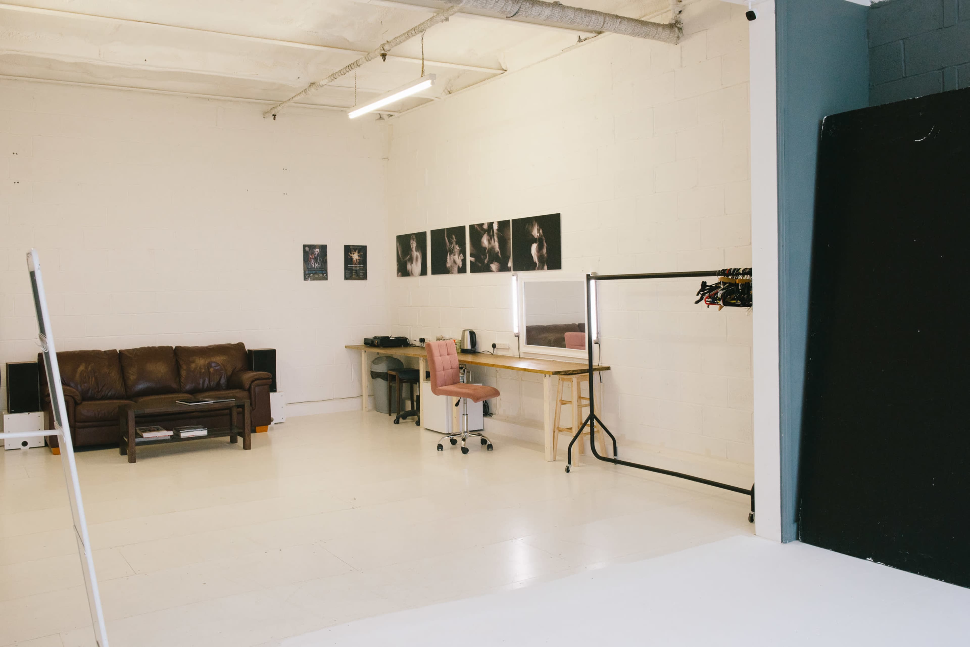A spacious, well-lit studio with a brown leather couch, a desk with office equipment, and a clothing rack along one wall.