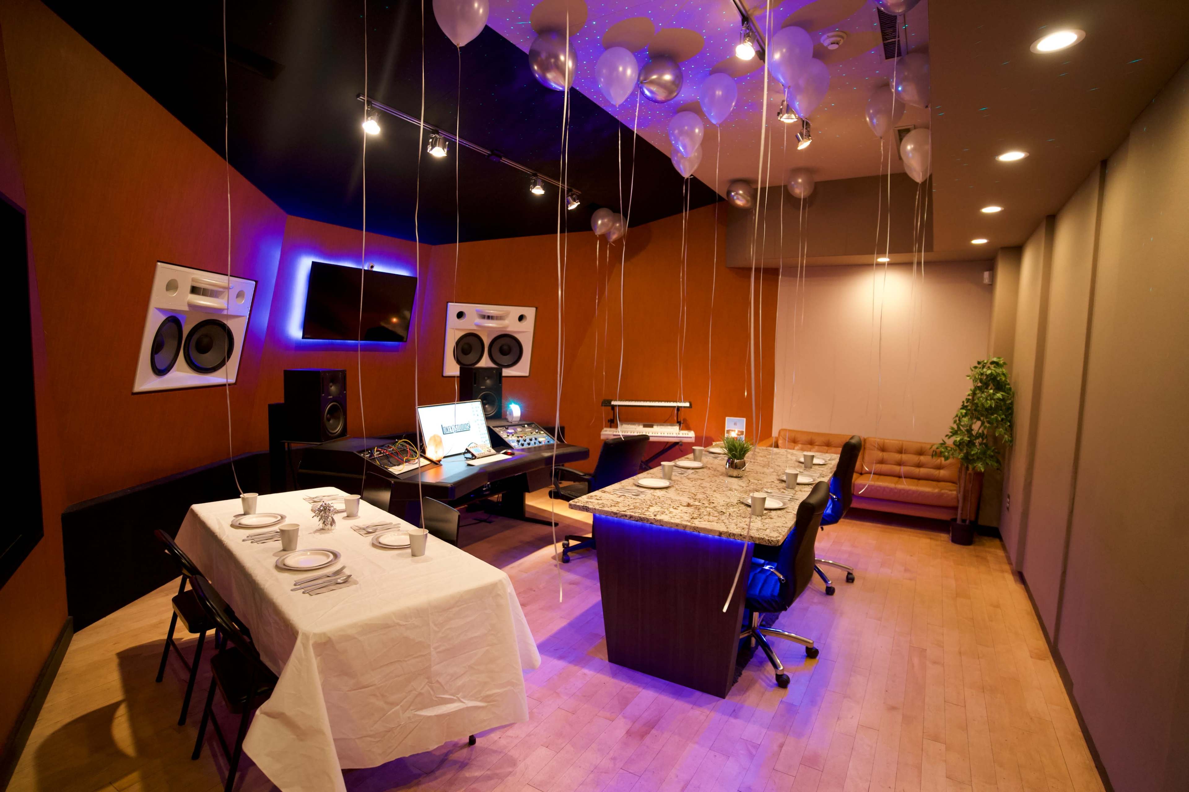 A modern recording studio featuring a large table set for dining, surrounded by sound equipment and decorated with balloons.