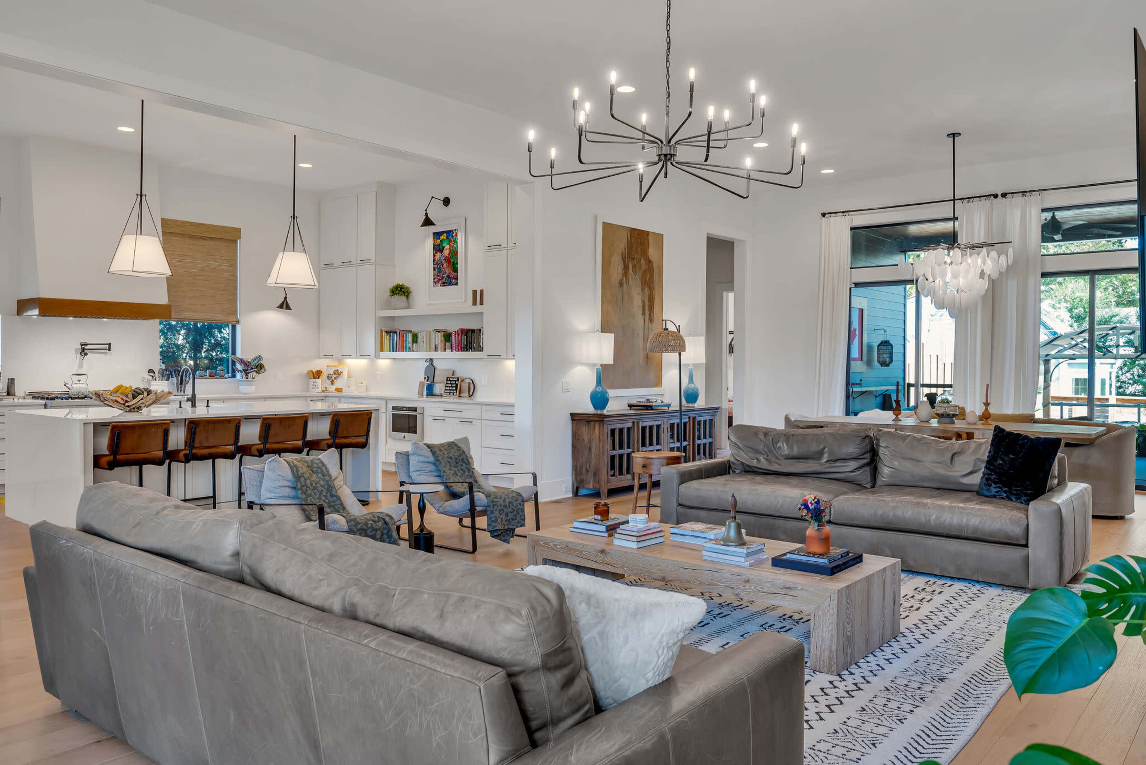 A modern living room with two gray sofas facing a wooden coffee table, a chandelier overhead, and an open kitchen visible in the background.