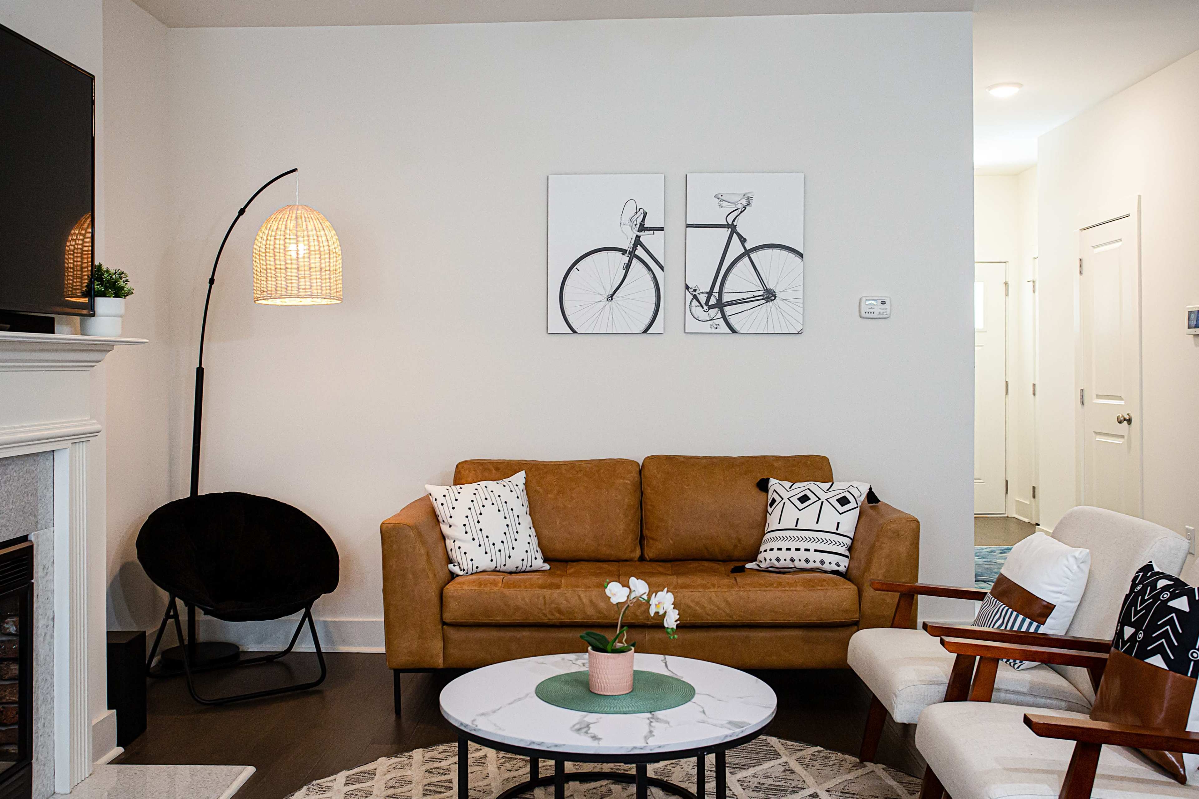 A modern living room featuring a brown sofa, a round coffee table with a plant, two armchairs, and wall art depicting bicycles.