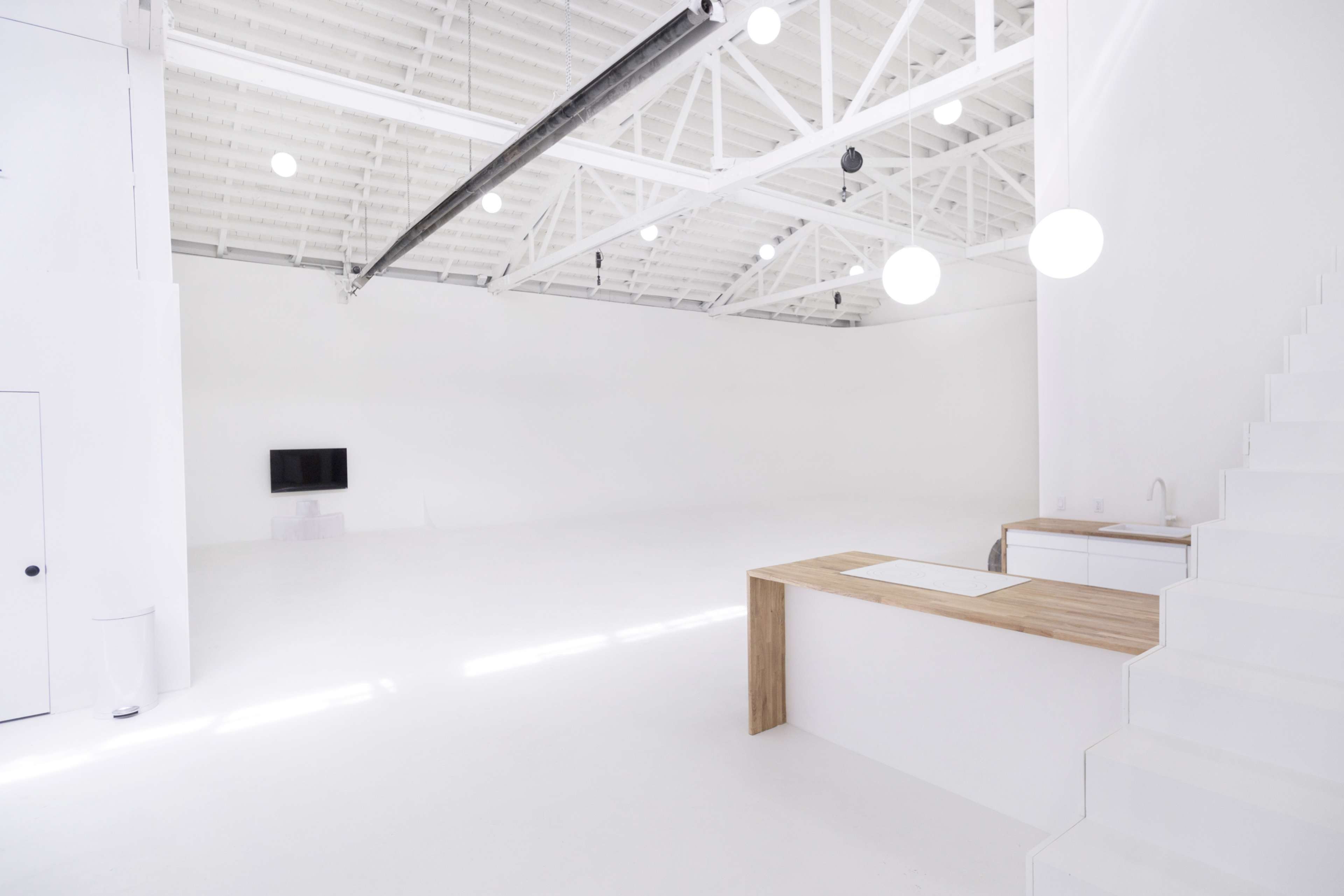 A spacious, well-lit interior with white walls, a simple kitchen island, and a staircase leading to a higher level.